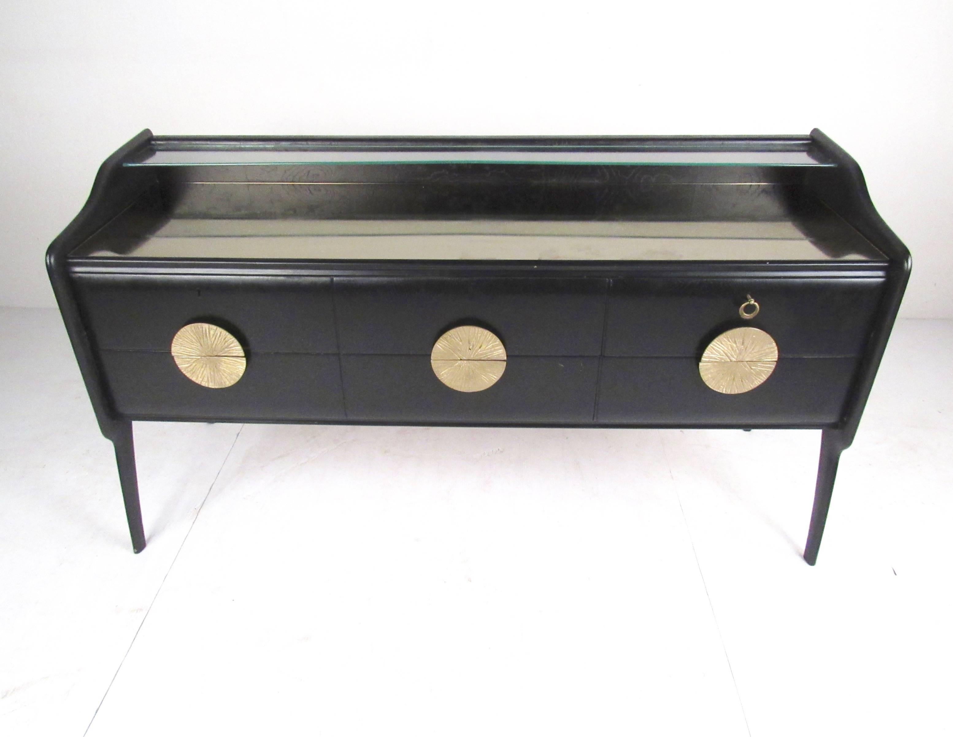 This unique vintage sideboard features two-tier glass top with small storage shelf built into the Italian modern design. Decorative brass finish pulls contrast wonderfully with the black finish. Six storage drawers with two locking make this an