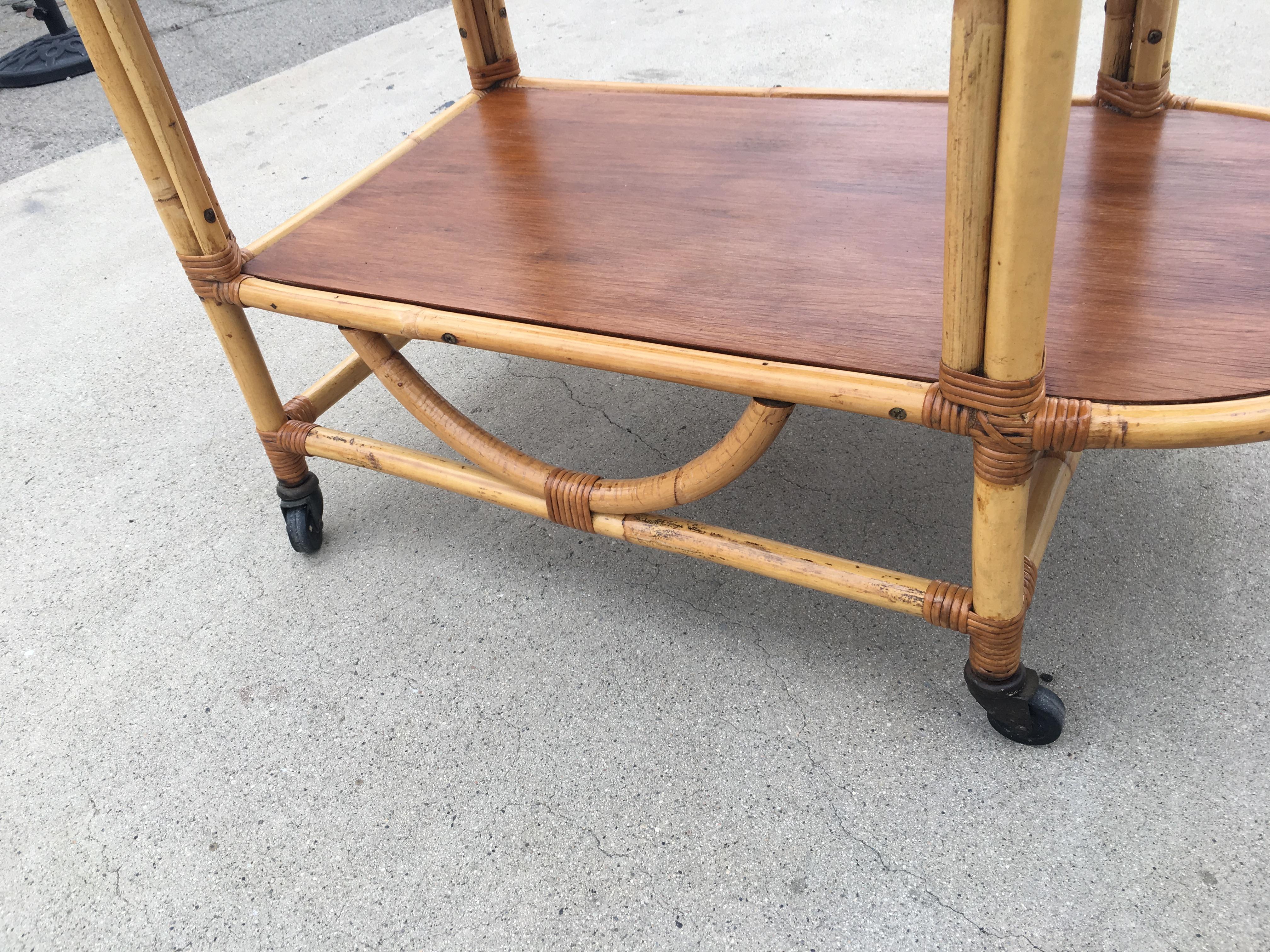 Unique 1950s bar cart features a u-shaped frame with two tombstone shaped shelves in mahogany and metal ball wheels.