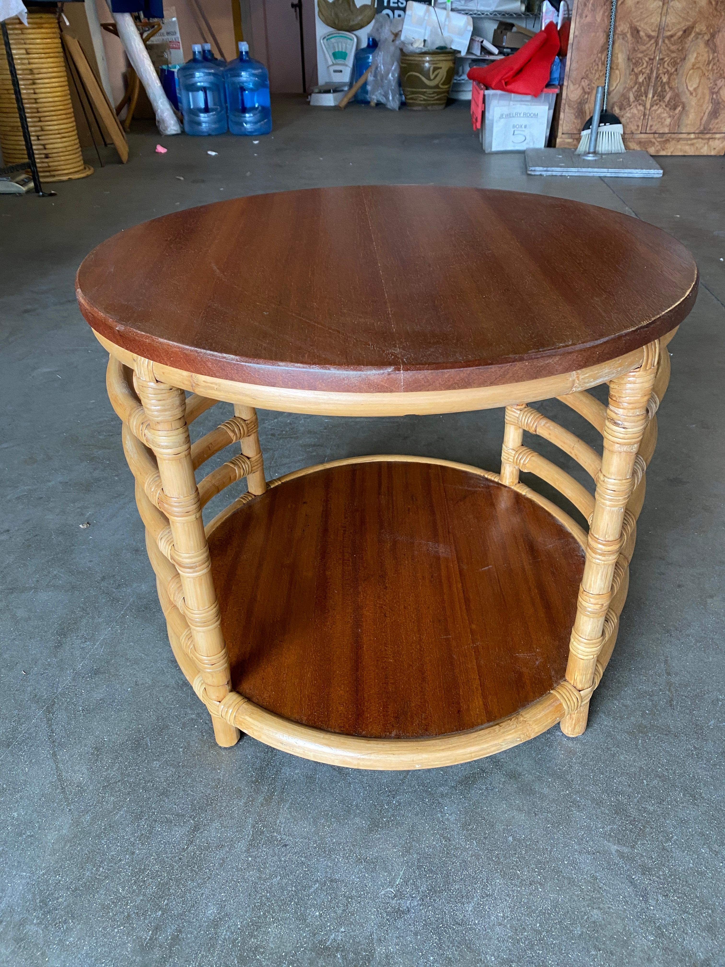 Postwar two-tier round rattan coffee table with twin mahogany tops and wrapped stick rattan ladder sides.
 
We only purchase and sell only the best and finest rattan furniture made by the best and most well-known American designers and manufacturers