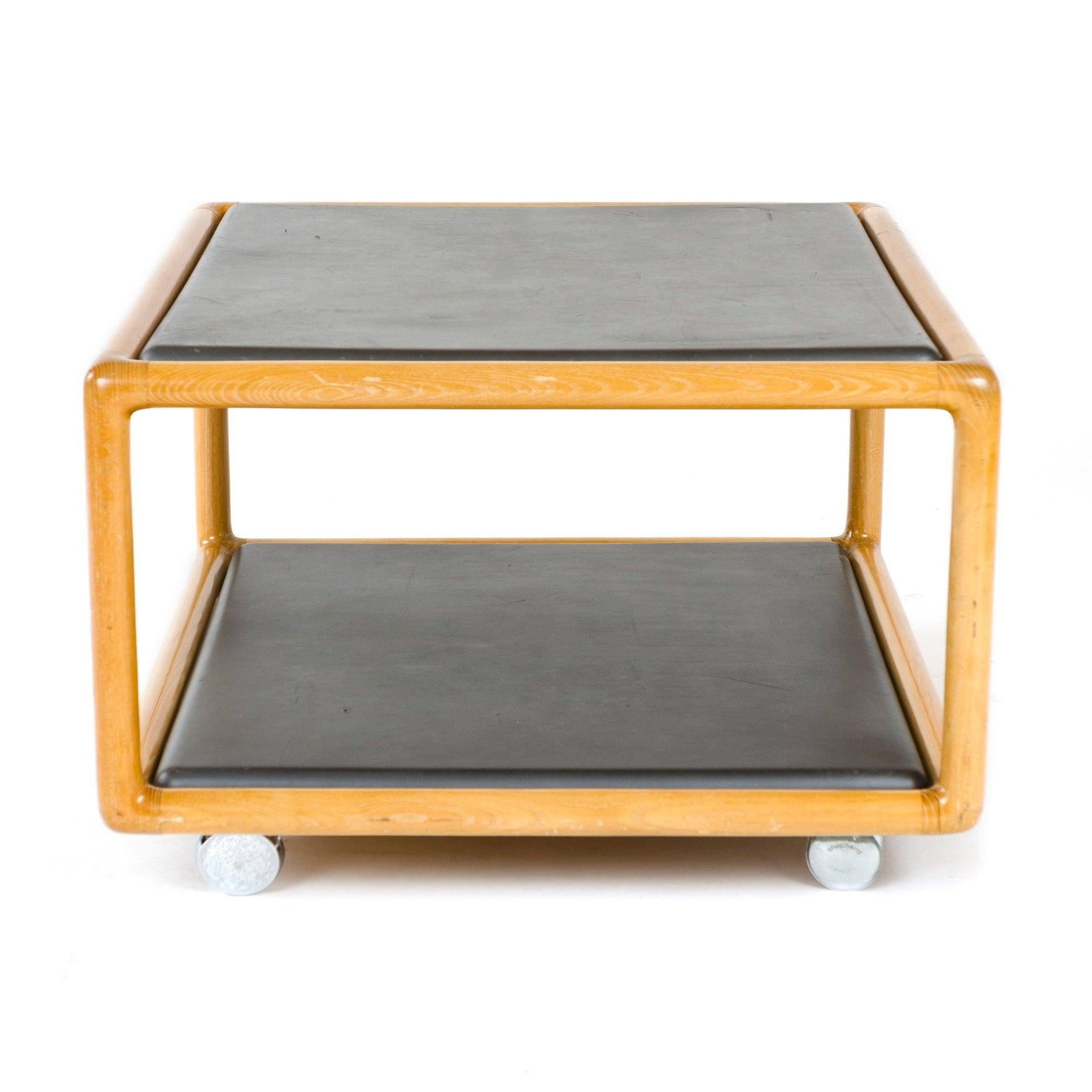 Mesa auxiliar o de centro de fresno tallado de dos niveles en acabado de aceite natural con superficies planas de piel Brickel sobre cuatro ruedas giratorias. Modelo 1260.