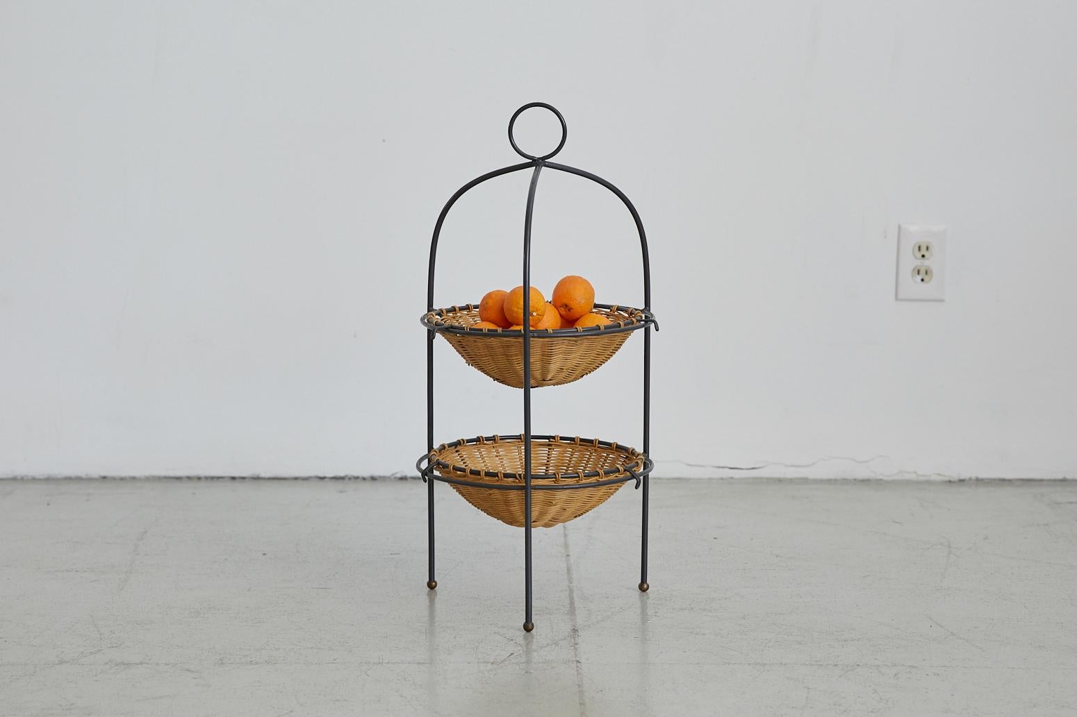 Beautiful two-tier French iron and wicker fruit basket. Two woven wicker removable baskets, curved iron frame with loop detailing at top, and three leg brass ball feet. Great center-piece for any table setting.

 