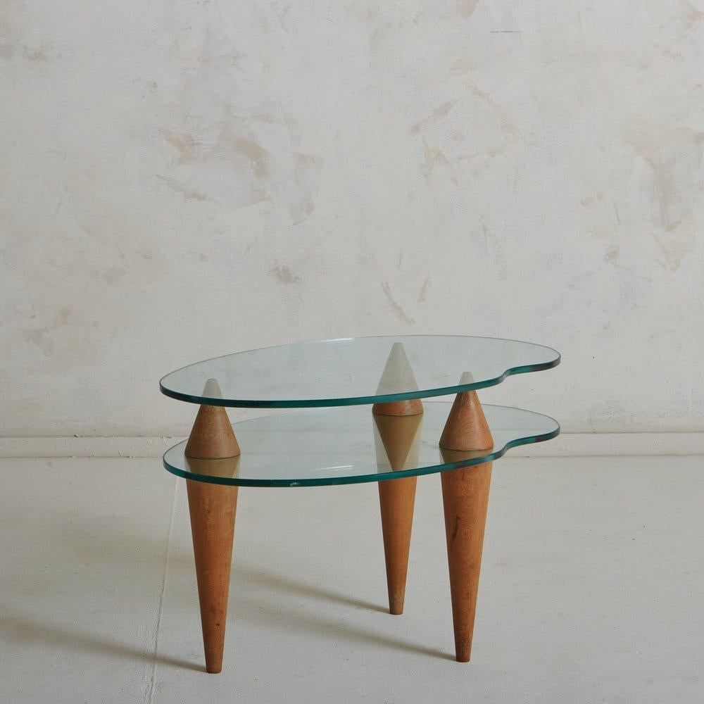 A sculptural Italian side table featuring two amoeba shaped glass shelves. The shelves are supported by three tapered wooden legs with triangular supports. We love the contrast between the sharp lines and delicate curves on this vintage beauty.
