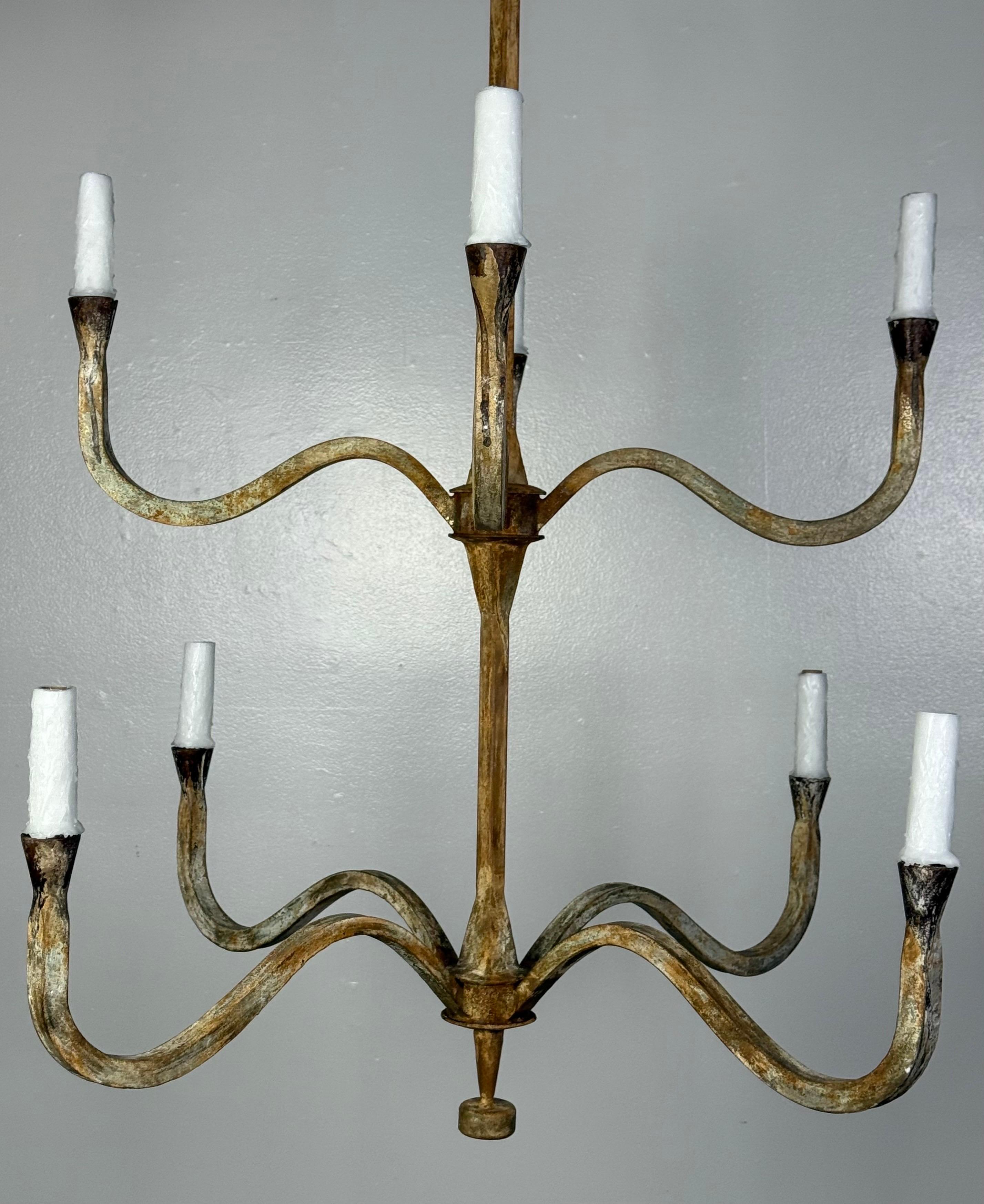 This two-tier, eight-arm iron chandelier features a graceful, sculptural design with subtly curved arms radiating from a central tapered hub. Each arm supports a white faux candle sleeve, adding a classic touch. The custom finish showcases a rich