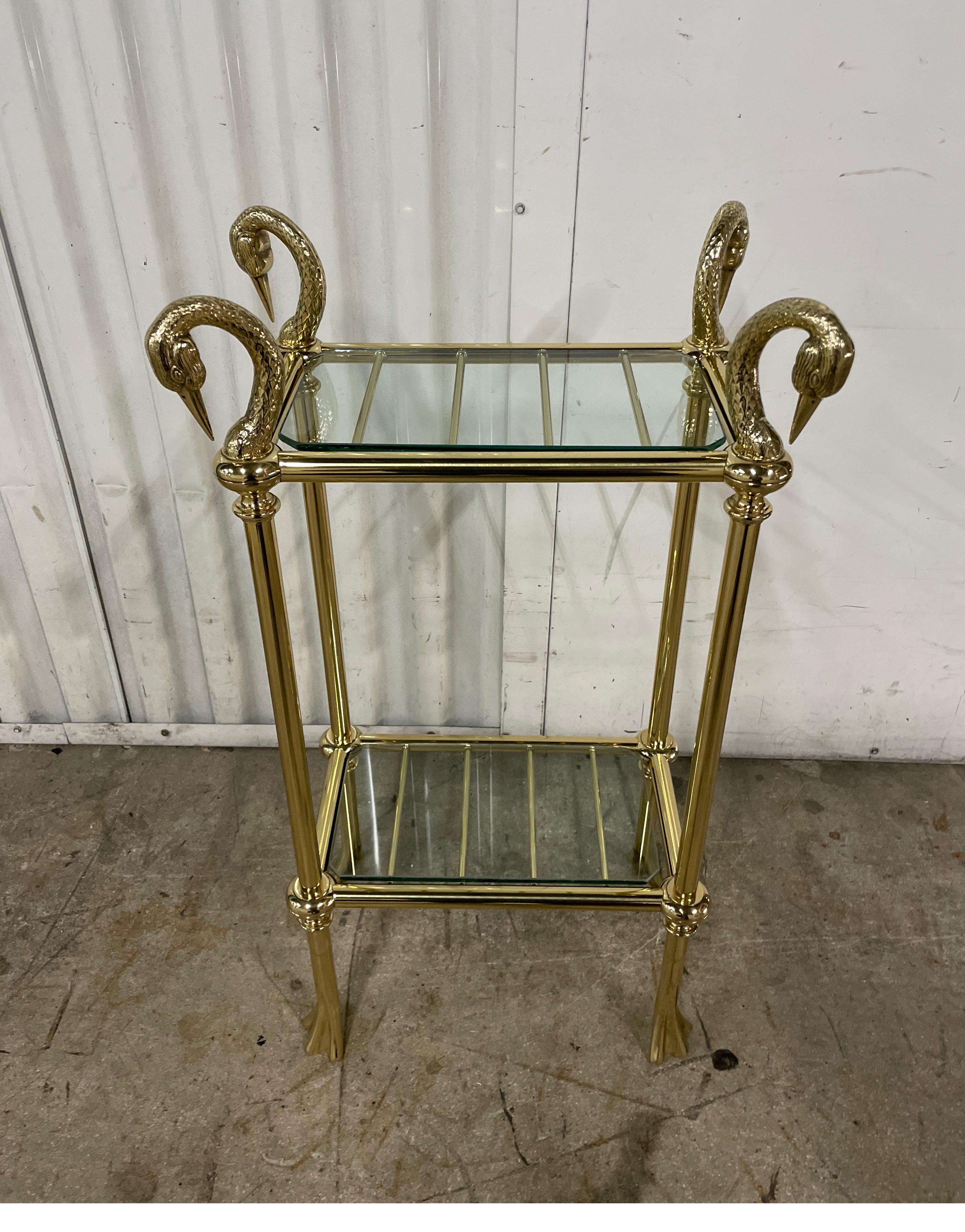 Exquisite brass two tiered stand with four Swan heads at top and Webb feet at bottom. Two glass shelves are held in place by brass rods. Wonderful chased details to swan heads.