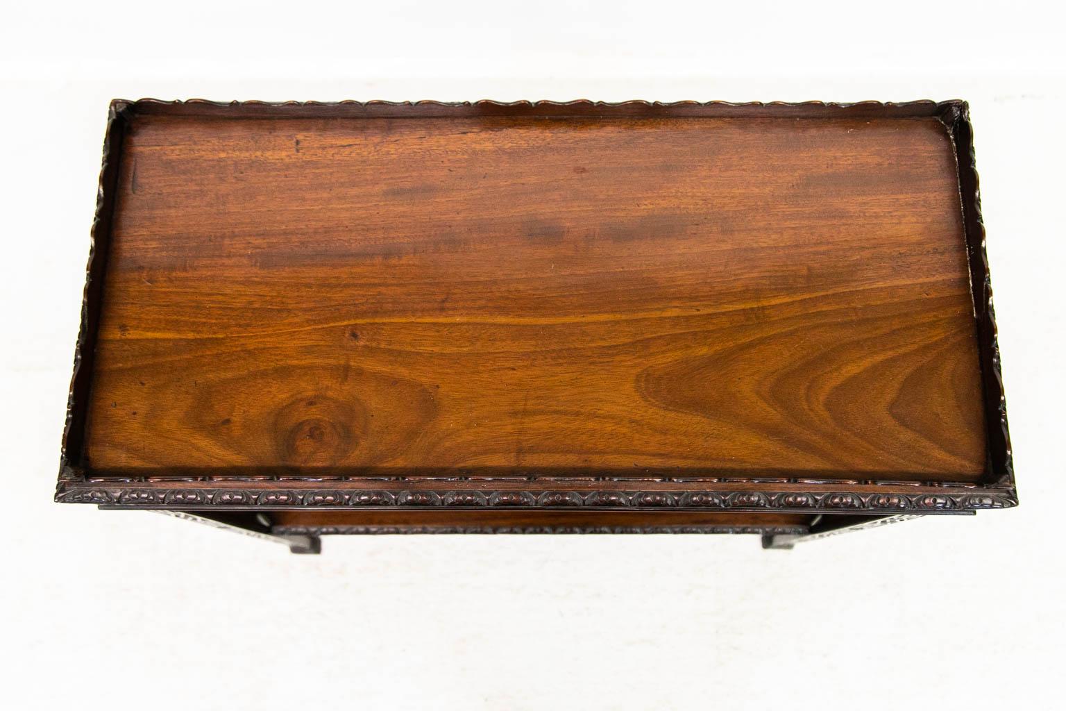 The top of this mahogany tea table has a scalloped gallery. The top edge has gadrooned carvings. The upper apron and legs are carved with blind fretwork. The lower shelf apron has carved floral arabesques. The inside of the legs are chamfered. One