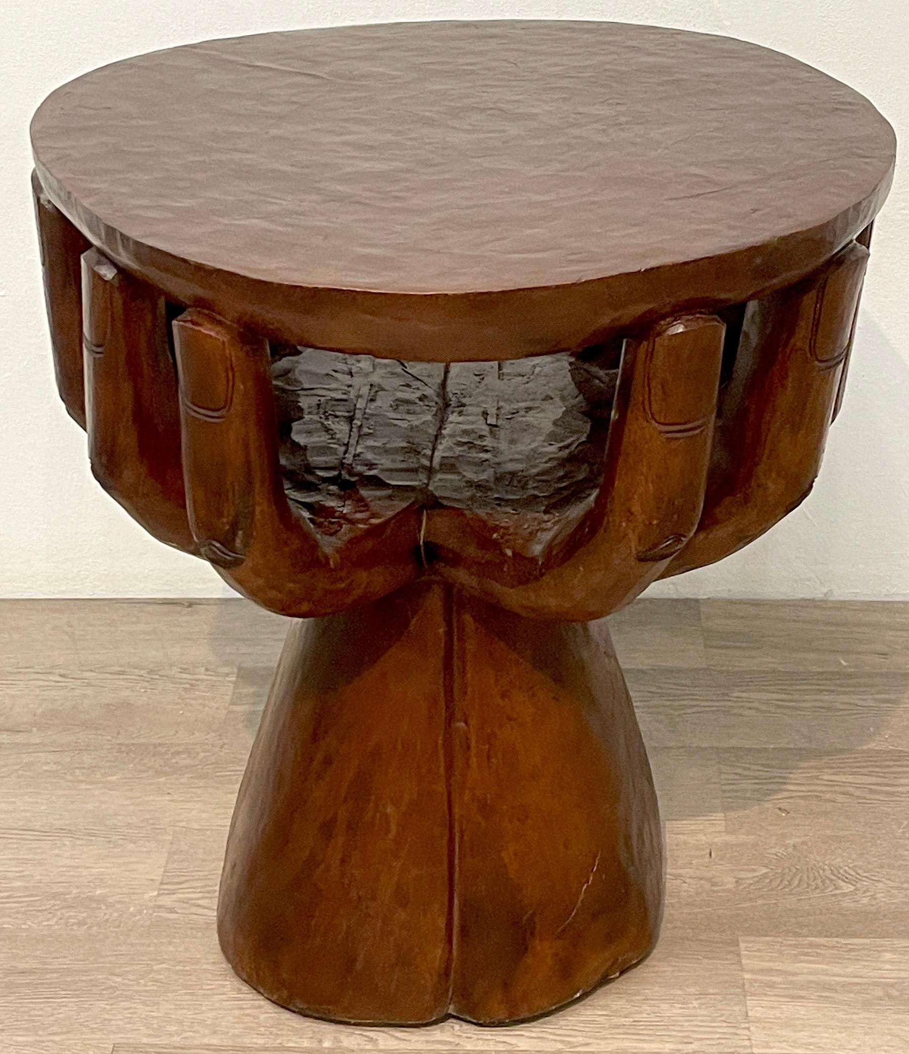 Two-tiered cupped hands table, in the manner of Pedro Friedeberg 
Well carved of hardwood, the 24.5-Inch diameter top resting on the fingertips of two hands, creating a 15-Inch deep x 12.5- Inch wide x 7-Inch high lower shelf. Raised on a 13-Inch