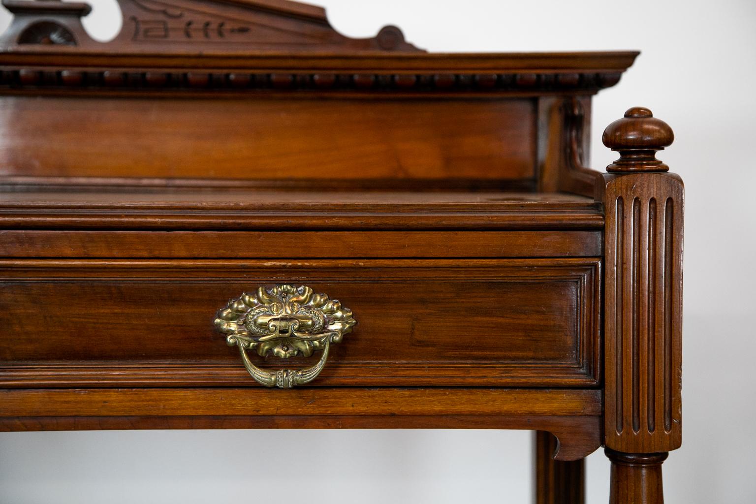 The back gallery of this two-tiered mahogany serving cupboard has a carved broken pediment top that rests on a crown molding that has carved egg and dart motif on the underside. The side galleries on the upper shelf have molded top edges that taper