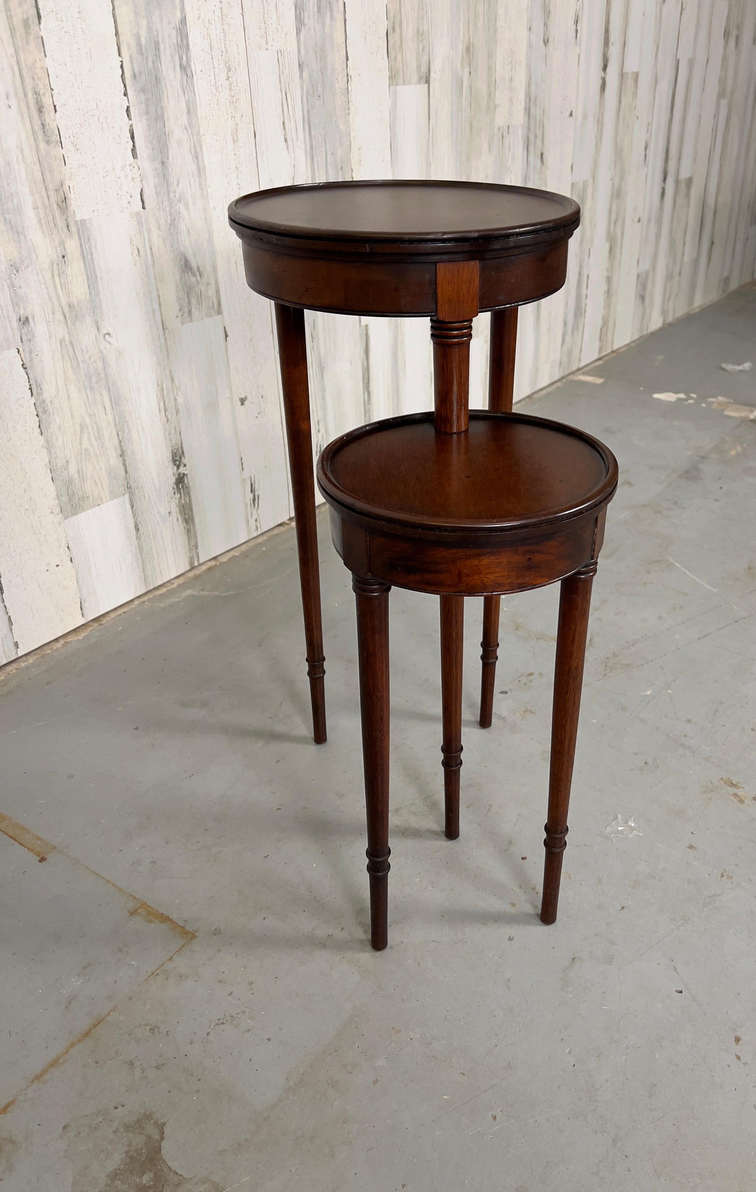 Two tiered candle stand that has two tables conjoined by one central leg that allows you to swivel the smaller table either underneath or out . 
 
