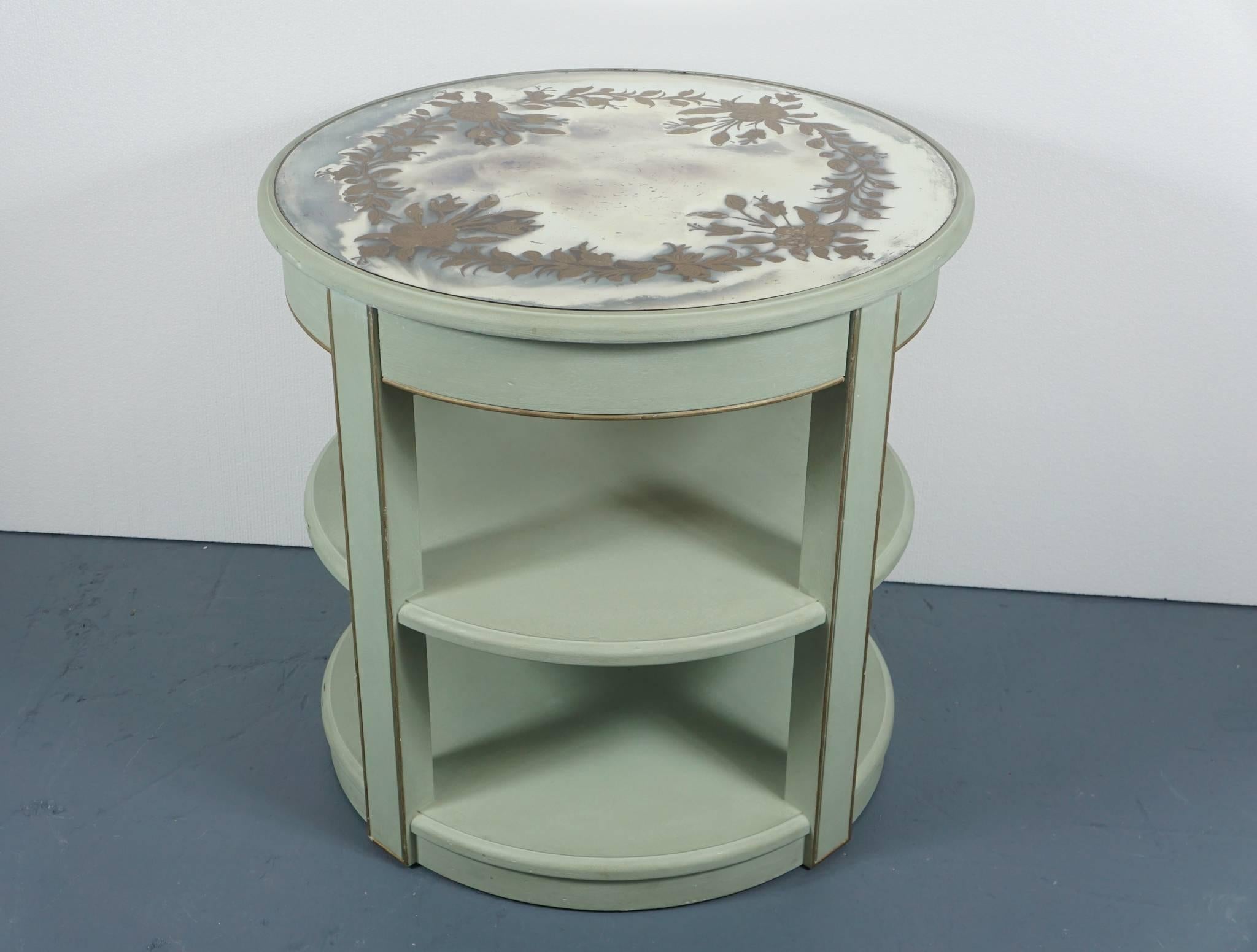 Here is an elegant two-tiered round table in a custom painted celadon finish with gold trim. The table top is an antique Églomisé with a gold painted flower and leaf motif. There is a centre drawer under the table top.