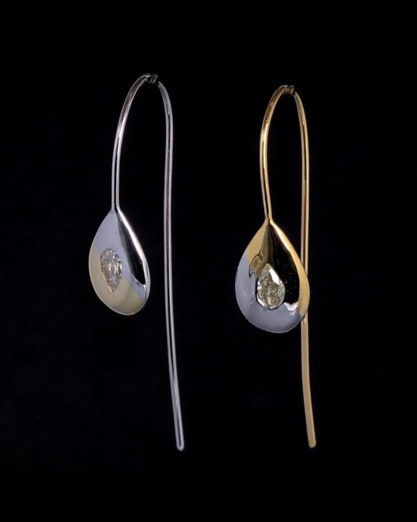 Two tone drop earrings with opposite but corresponding gold and diamond colors. One earring has a white gold base with a white diamond pear shape and yellow gold accent, while the other has a yellow gold base with a yellow diamond pear shape and a