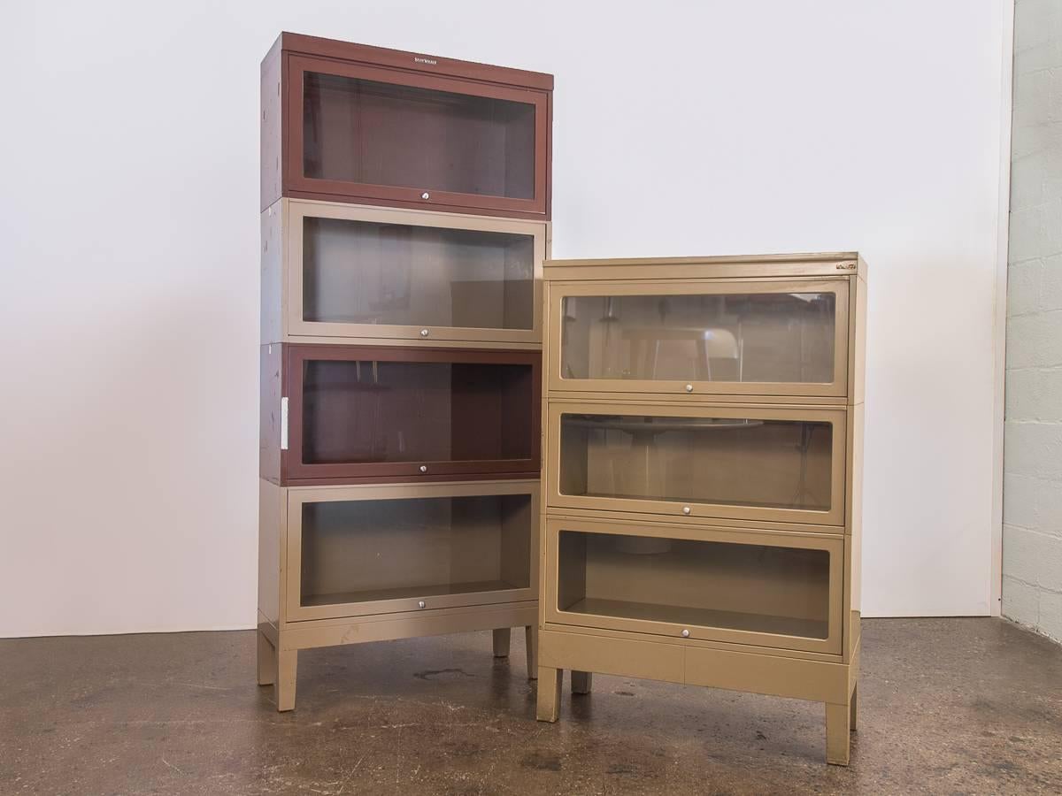 Vintage 1960s metal barrister stacking bookcases for Shaw Walker. A versatile and sturdy cabinet for all your storage needs. This set is comprised of four modular, stackable bookcases with a base and top cover. Each unit has a sliding glass door for