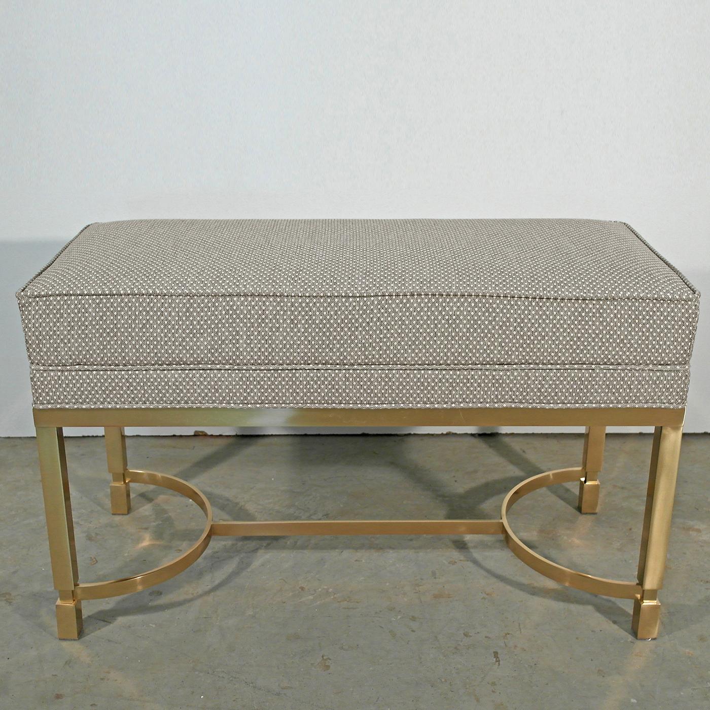 This elegant bench boasts a brass base with a polished finish, characterized by semi-circular details for a modern look. Its padded seat is upholstered in soft fabric with a subtle two-tone motif. With its sleek lines and muted hues, the two-tone