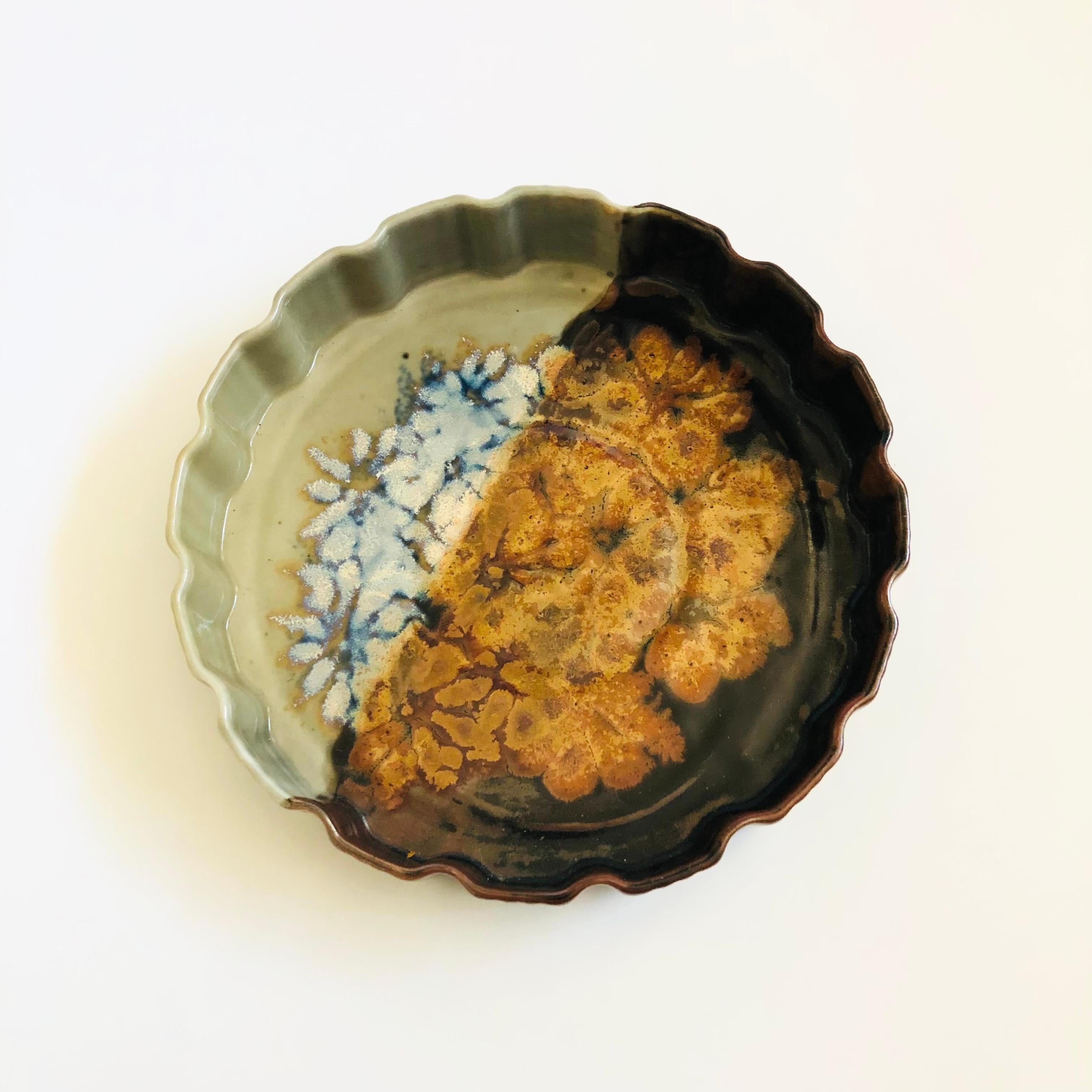 Un grand plat à quiche vintage en poterie de studio. Magnifique glaçure de couleur terre et bord festonné. Motif floral peint à la main au centre.

