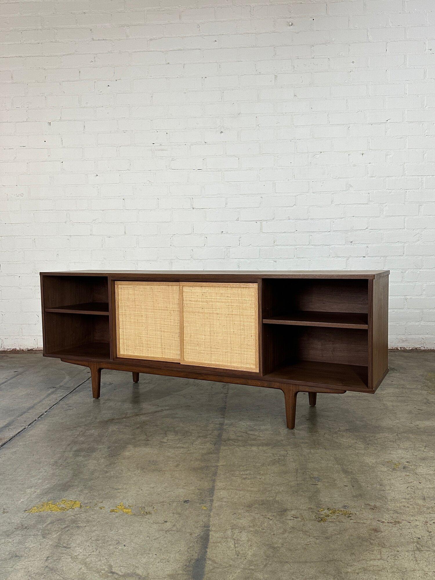 W72.5 D16 H27.5

Two toned Custom made credenza made from a mixture of solid wood and walnut veneer. Credenza features symmetrical design with a shelf on each side and two white oak cane paneled sliding doors that slide to reveal another