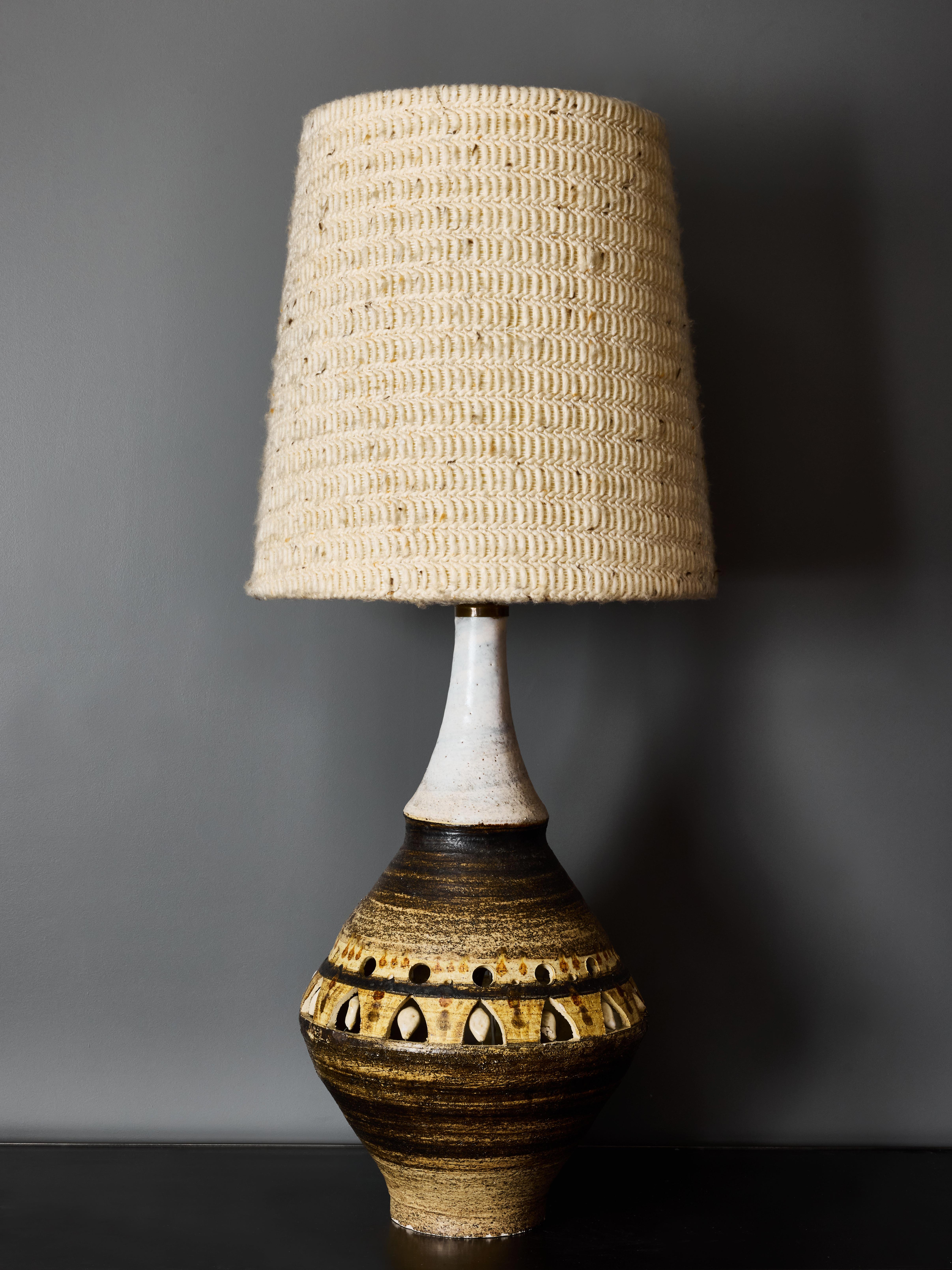 Large ceramic table lamp designed by George Pelletier features the top half finished in white glaze while the bottom part showcases the distinctive artist’s brown-beige matte glaze adorned with openwork decorations that allow the inner light to