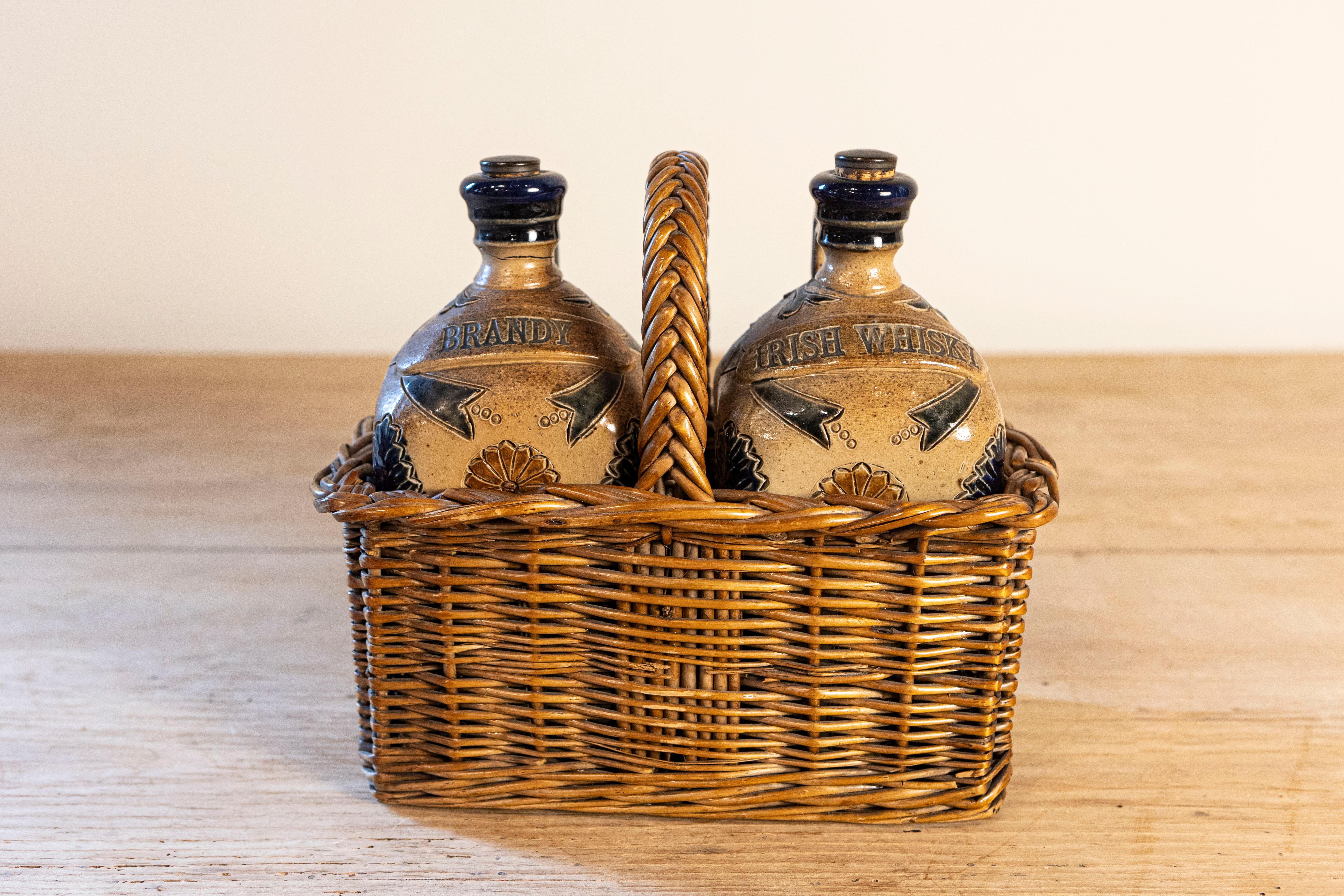 Two English pottery decanters in a tantalus inspired wicker basket from the mid 19th century. Born in England during the Victorian period, this pair of decanters is set inside a tantalus-inspired wicker basket, adorned with a woven handle.