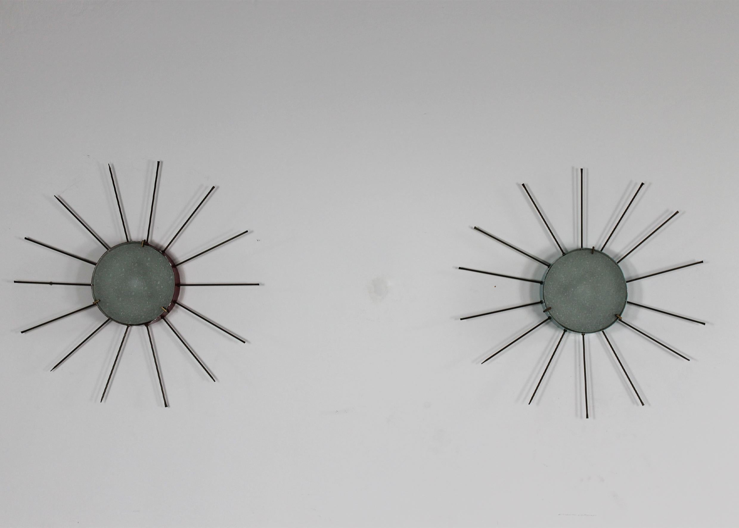 Set aus zwei Wandlampen (sie können auch als Deckenlampen verwendet werden) mit Struktur aus lackiertem Metall (eine mit hellblauem und eine mit leuchtend rotem Schirm), geprägtem Glas und Details und handgefertigten Spikes aus Messing.
Diese Lampen