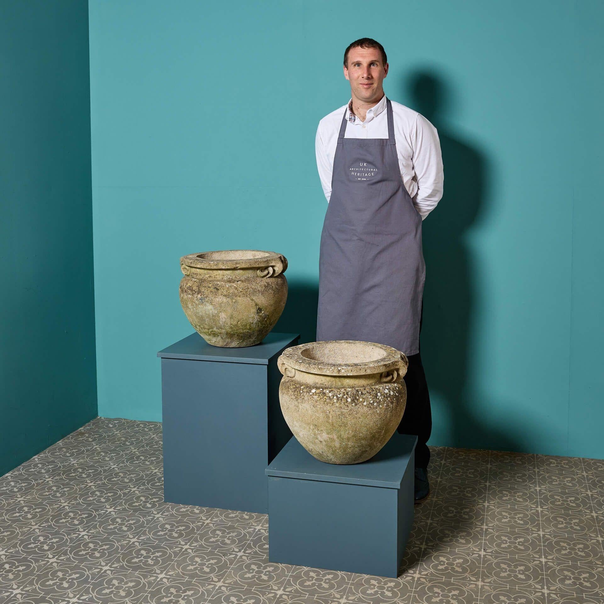 A pair of reclaimed and beautifully weathered Compton style scroll pots, robustly cast in composition stone that resembles a light Portland limestone.

These large planters are of the same scale and design, the thick top edge and scrolling handles