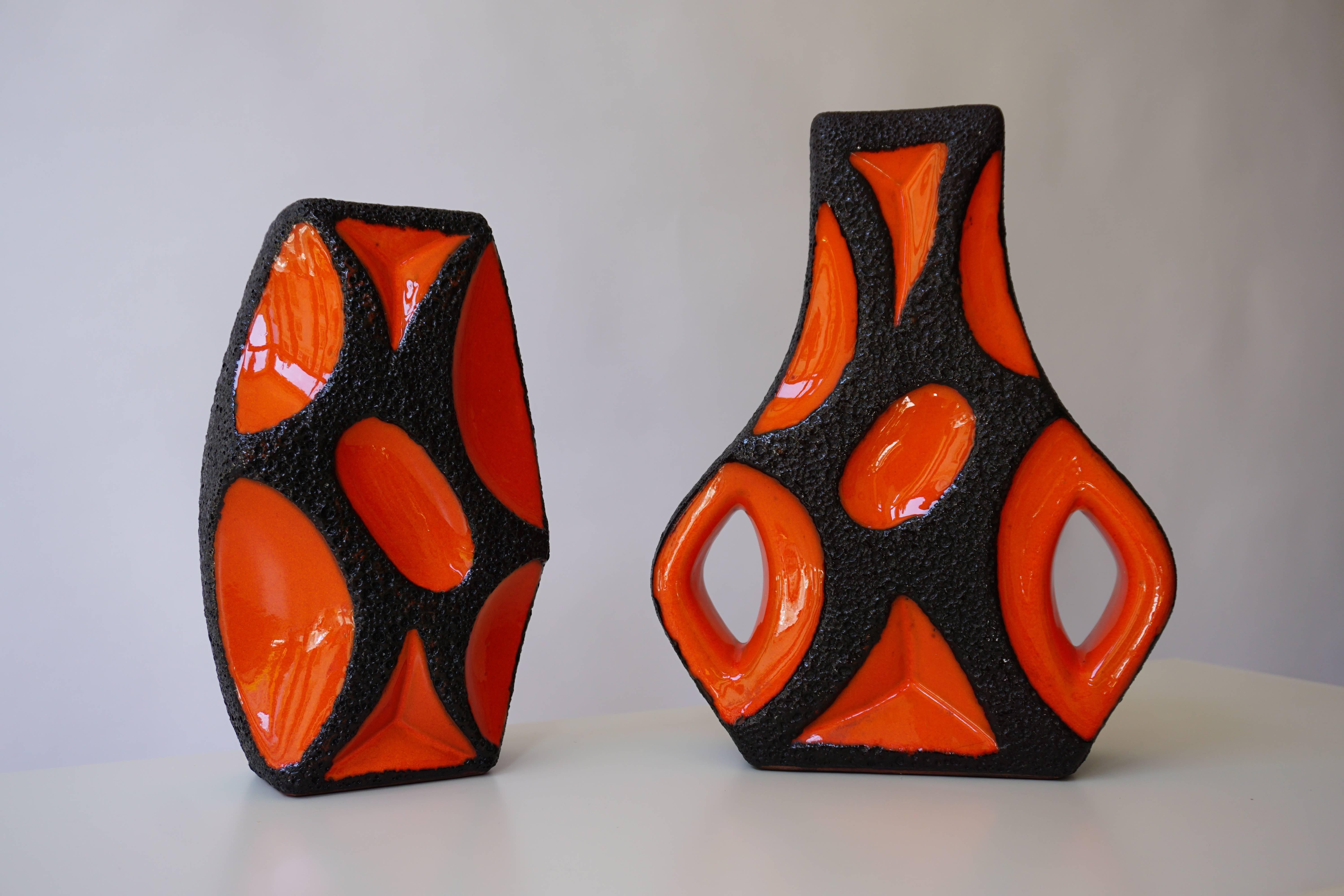 Zwei Vasen aus westdeutscher Roth Keramik mit orangefarbener Glasur; Gitarrenvase mit quadratischer Öffnung über einem bauchigen Körper, alles in einer dicken Lavaglasur mit orangefarbenen Glasurreserven.
Maße: Höhe 31 cm und 27 cm.
Breite 25 cm