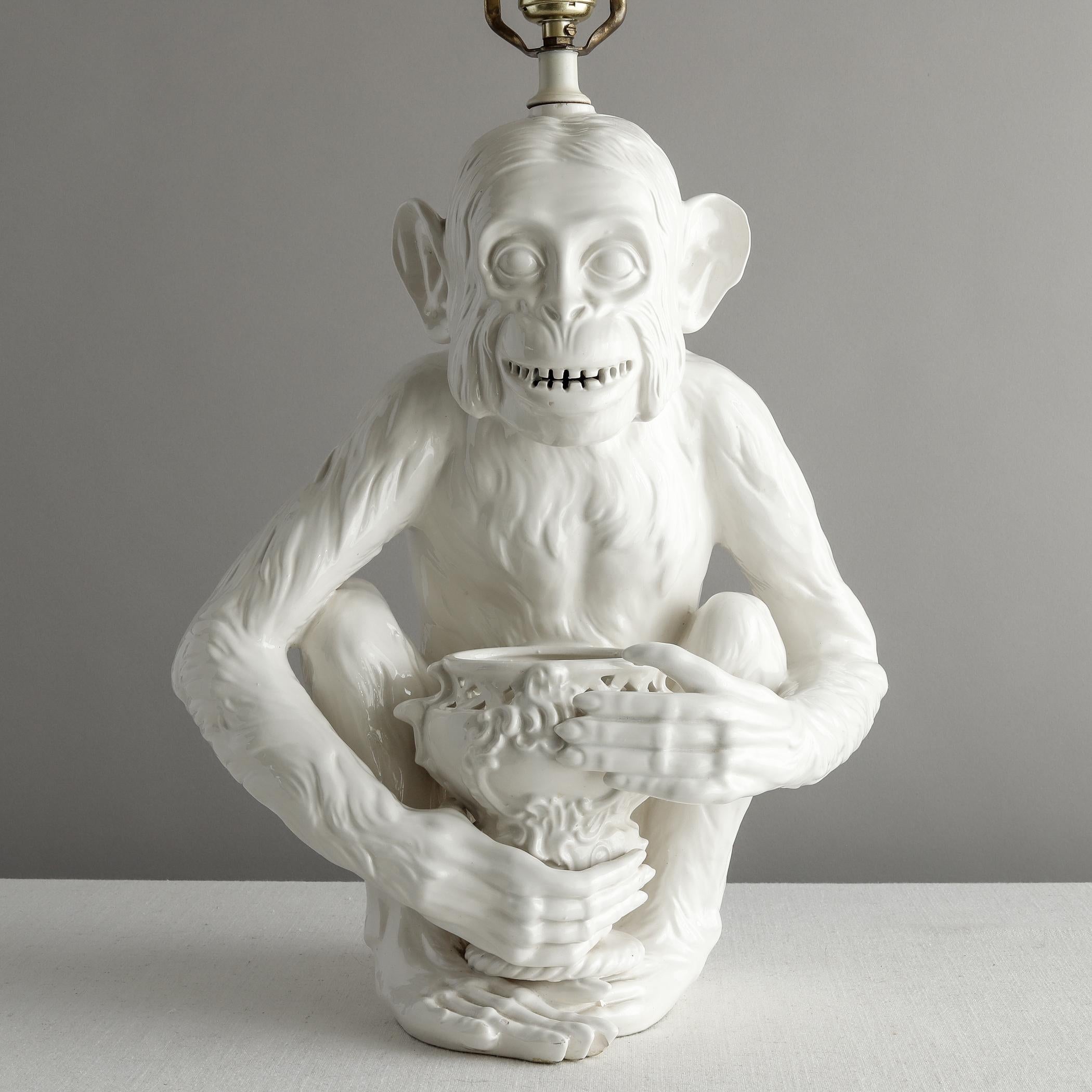 Two white glazed ceramic table lamps, probably Italian, each in the form of a different seated monkey. One, a chimpanzee, holds a Rococo-style vase (which looks like it should be able to hold flowers). The other appears to be a type of macaque and