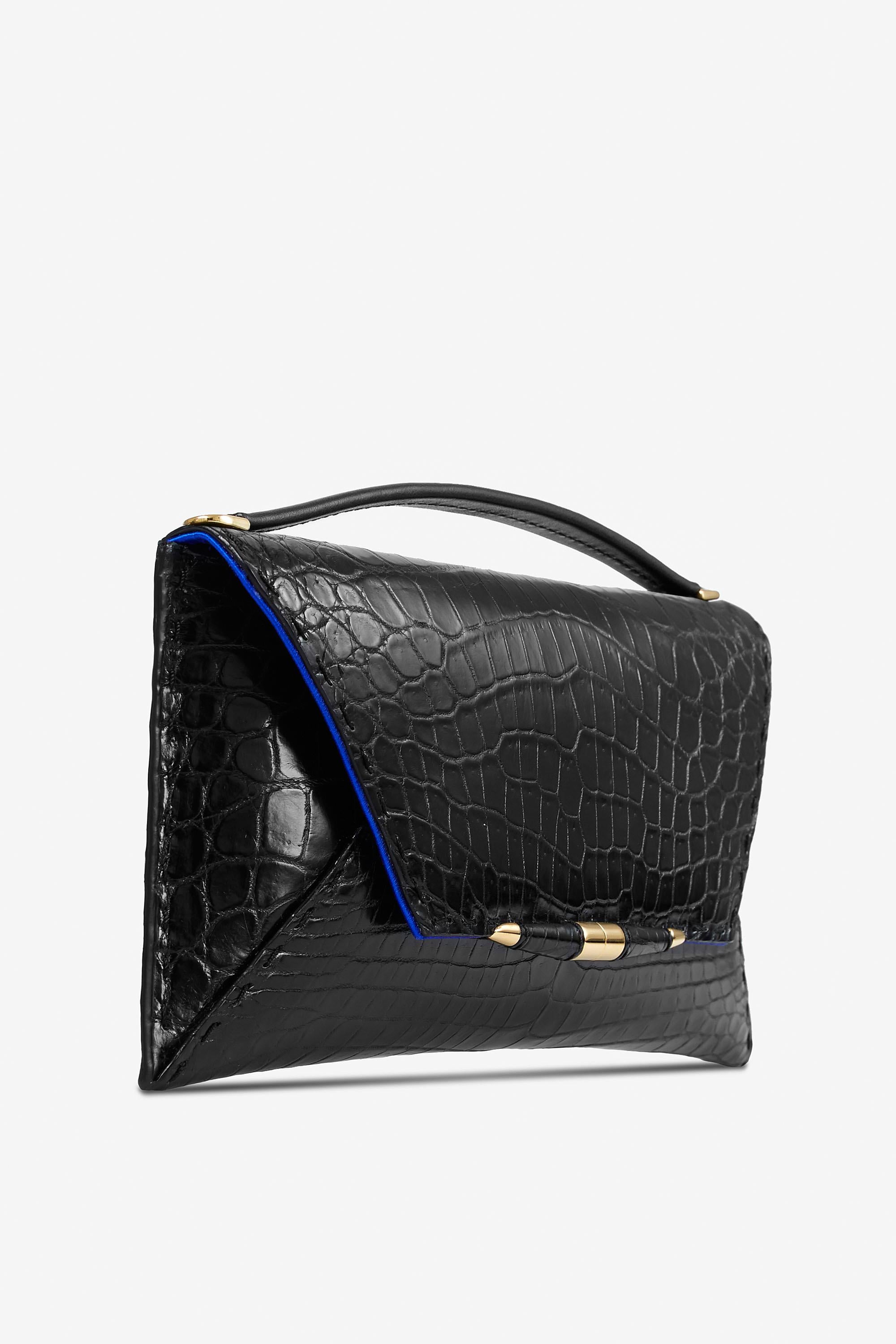 The Aimee Clutch Large Black Noir Crocodile Gold Hardware is designed with a magnetic front flap snap closure, hidden exterior pocket and a detachable cross-body Black Alligator strap. It features our custom infinity bar closure and signature Thayer