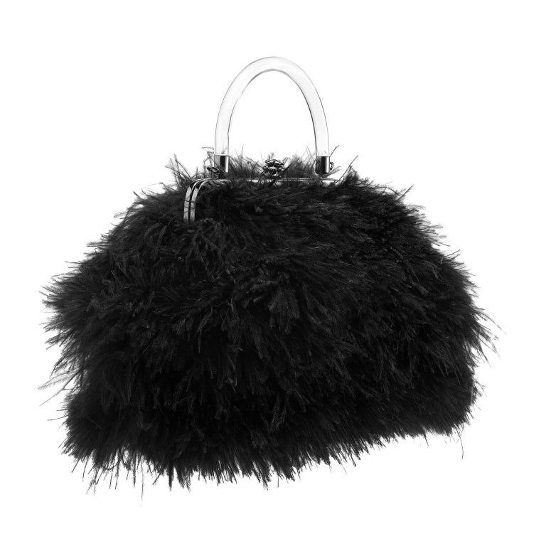 The Poppy handbag small is featured in black ostrich feathers with gunmetal detail. This soft handbag is designed with a Lucite handle and our custom half-metal frame topped with our Pinecone Closure. It fits the large iPhone has a detachable metal