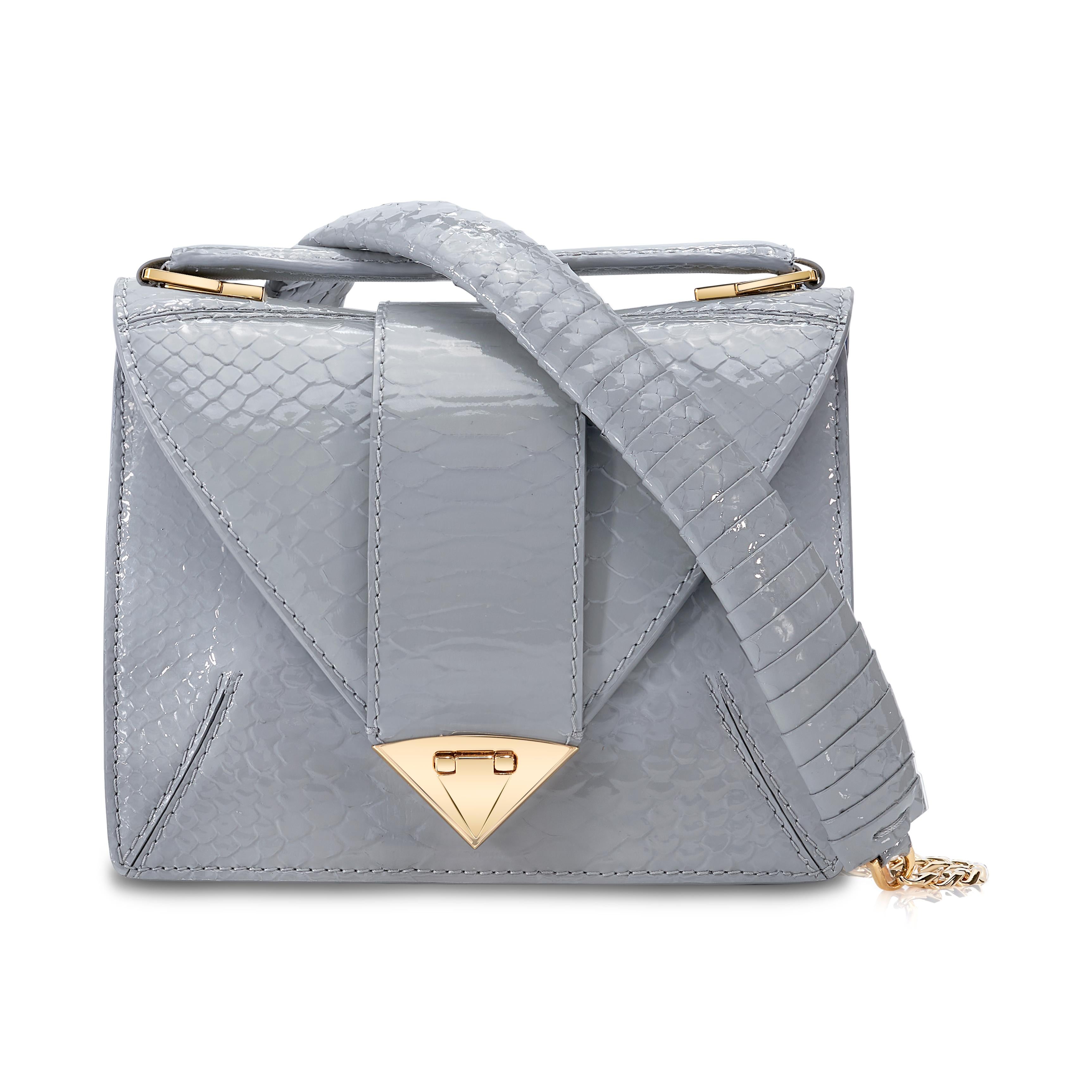 The Rita in Dove Grey Glossy Python is a semi-structured handbag with a triangular front flap finished with our custom Spear-lock Closure. It is designed with a flexible top handle and an optional gold chain with a python accent.  It fits the large