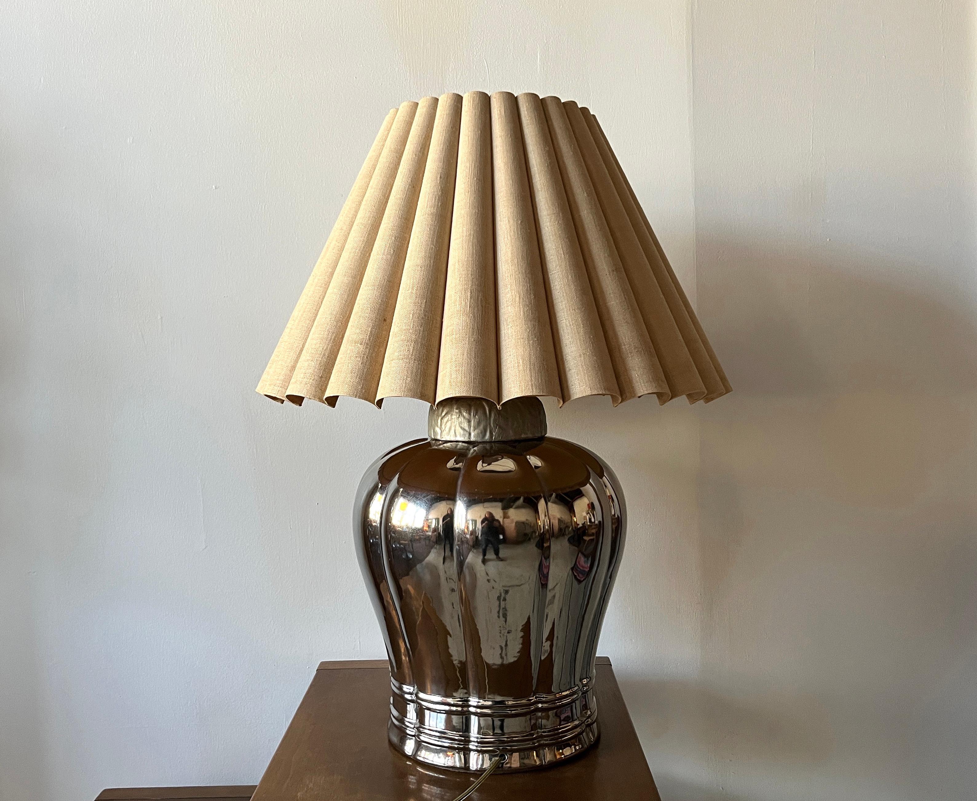 Manufactured in Chicago, Tyndale lamps continue to be some of the most coveted antique light fixtures on the market. This monumental example in mercury glass with a bulbous, ribbed shape features its original pleated linen shade with the warmest