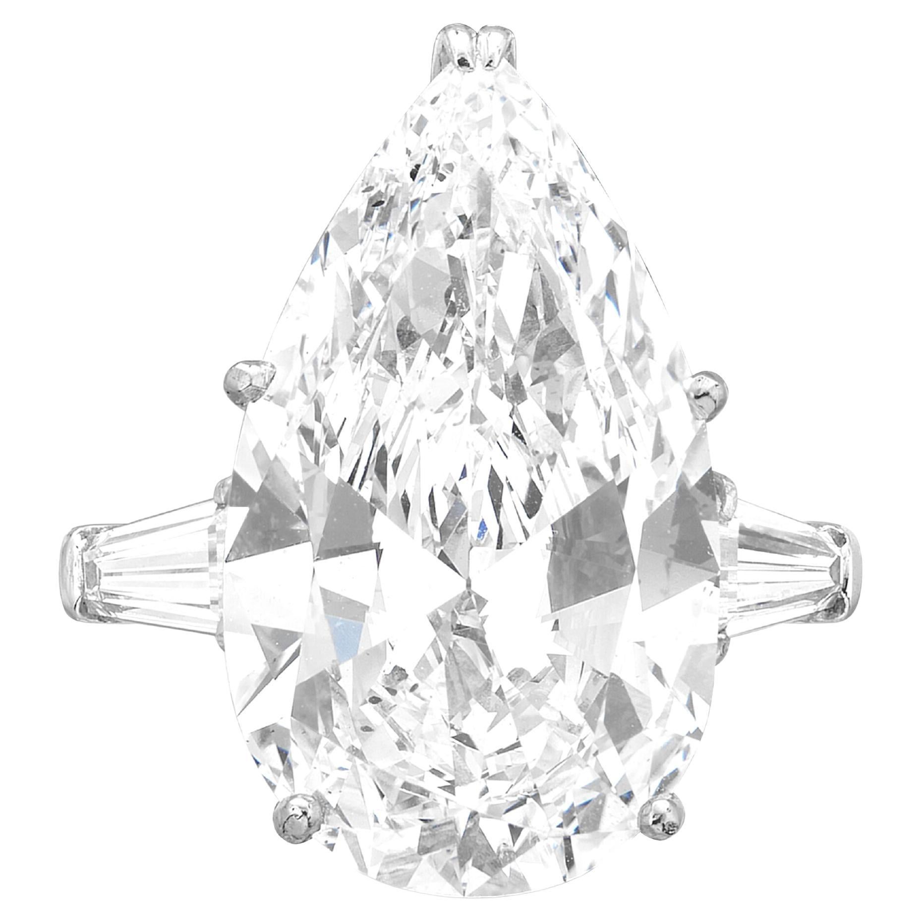 Obra maestra de refinamiento y artesanía, este anillo de compromiso de platino con tres piedras es un testimonio de perfección. En su centro brilla un extraordinario diamante natural talla brillante en forma de pera de 5 quilates. De color D, el