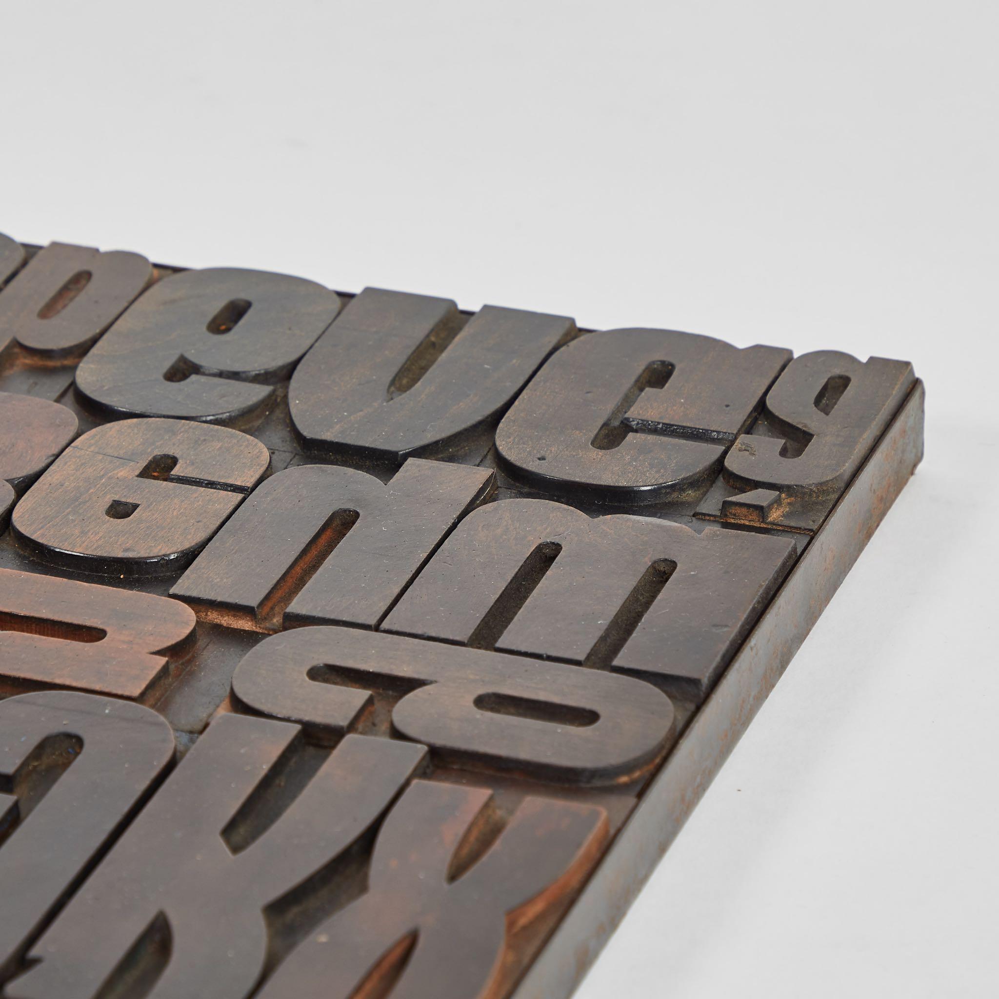 Typeset tray from an early 20th-century French printing press with a series chunky wooden alphabetical blocks narrowly arranged in a flat, rectangular metal holding tray. Graphic yet sculptural, the item could be displayed a number of ways, and with