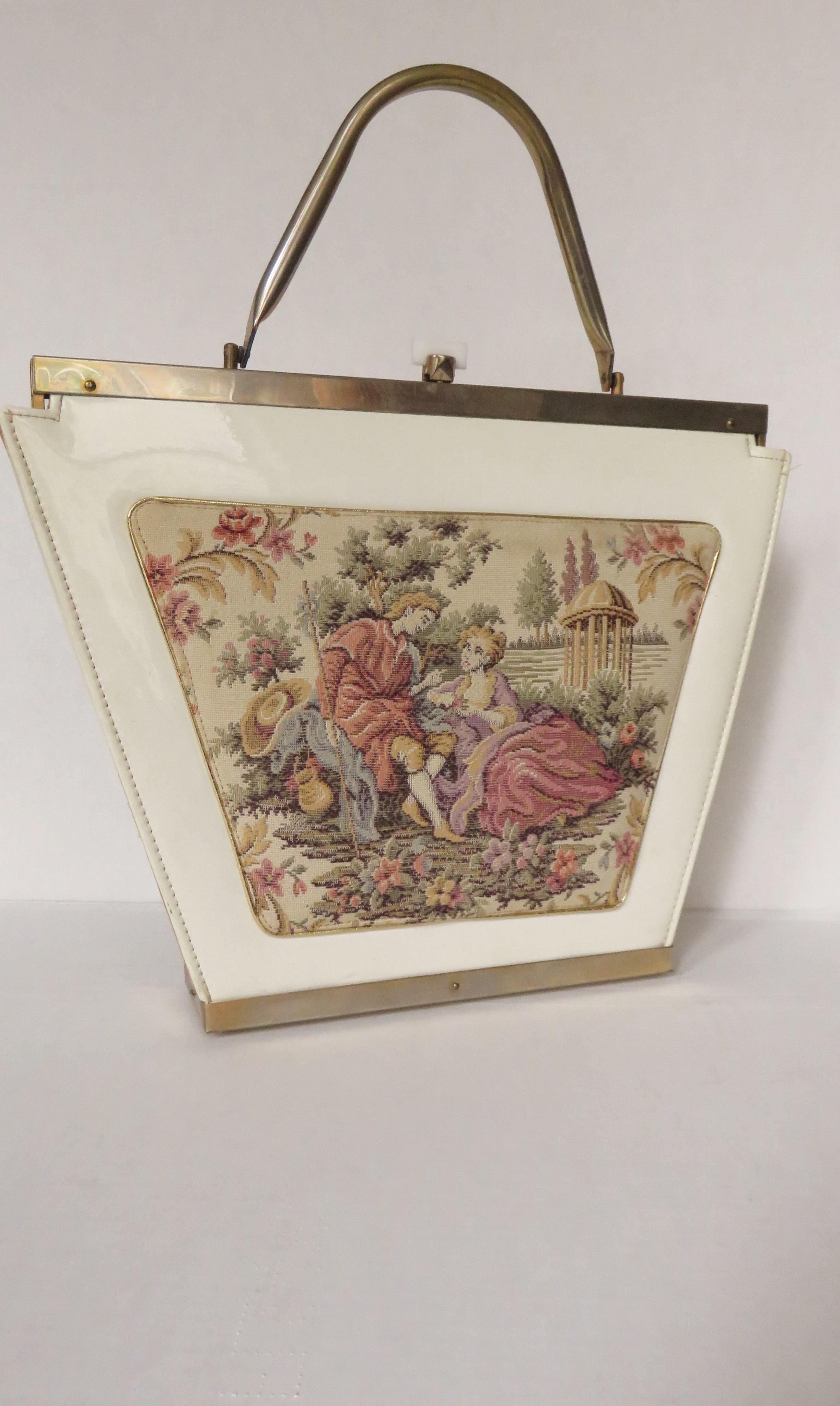 A fabulous large white patent triangular shaped handbag with a front padded tapestry applique of an 18th century man and a woman outlined in gold.  It has a gold clasp with white bar, a tubular gold metal handle matching the frame top and bottom.