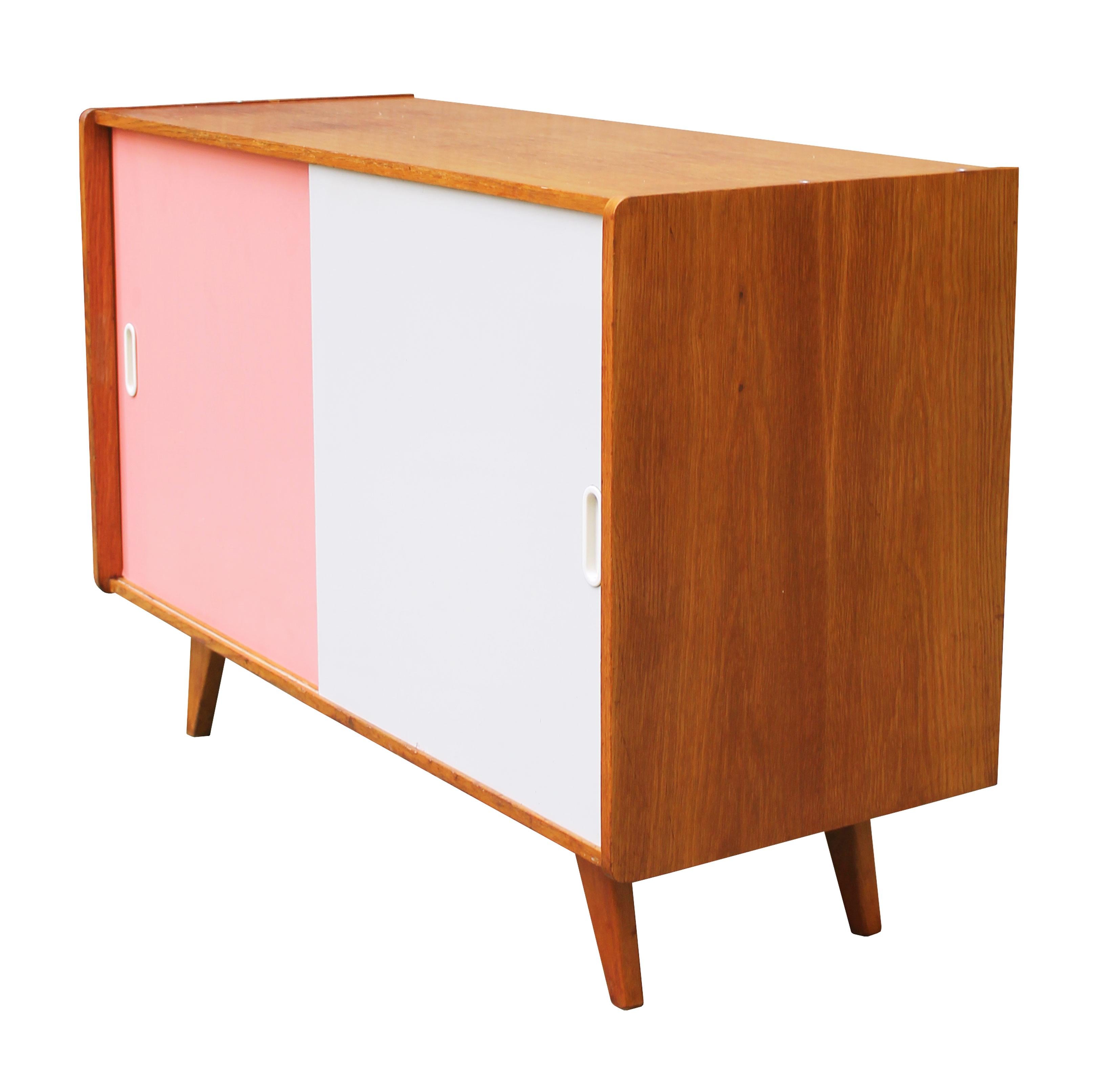 The U-452 mid-century sideboard with pink and white sliding doors, was designed by the Czech furniture designer Jiri Jiroutek. It is part of the popular U collection manufactured by Interier Praha in the 1960s Czechoslovakia. 

This piece perfectly