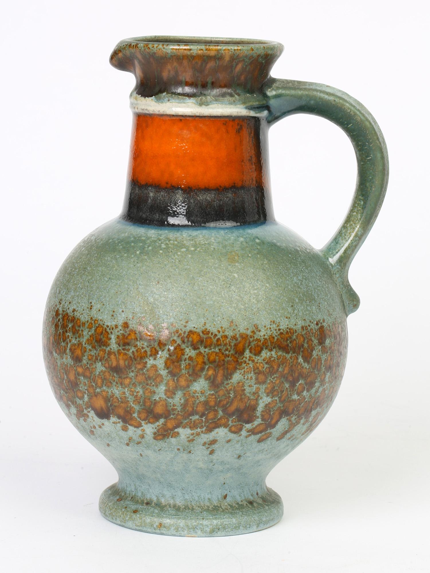 A very finely made midcentury West German art pottery handled vase decorated in 'fat lava' glazes by Uberlacker and dating from circa 1960. The ceramic vase is made to emulate a jug with a fake shaped pouring spout and with a loop handle to the