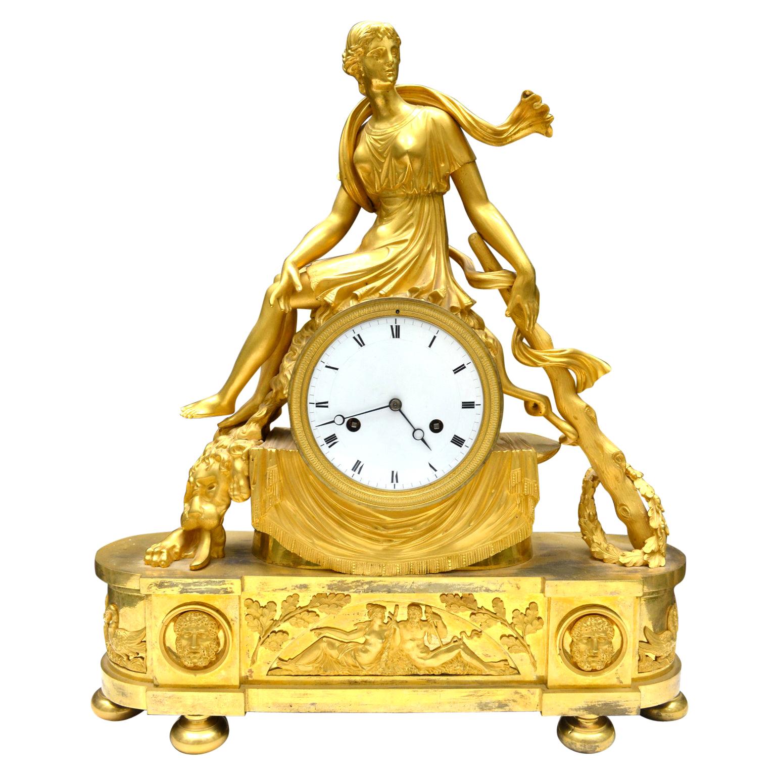 Pendule Empire en bronze doré du début du 19e siècle représentant la reine mythologique lydienne Omphale assise à califourchon sur un tambour drapé qui contient le cadran et le mouvement de la pendule. Omphale est représentée avec la toison du lion