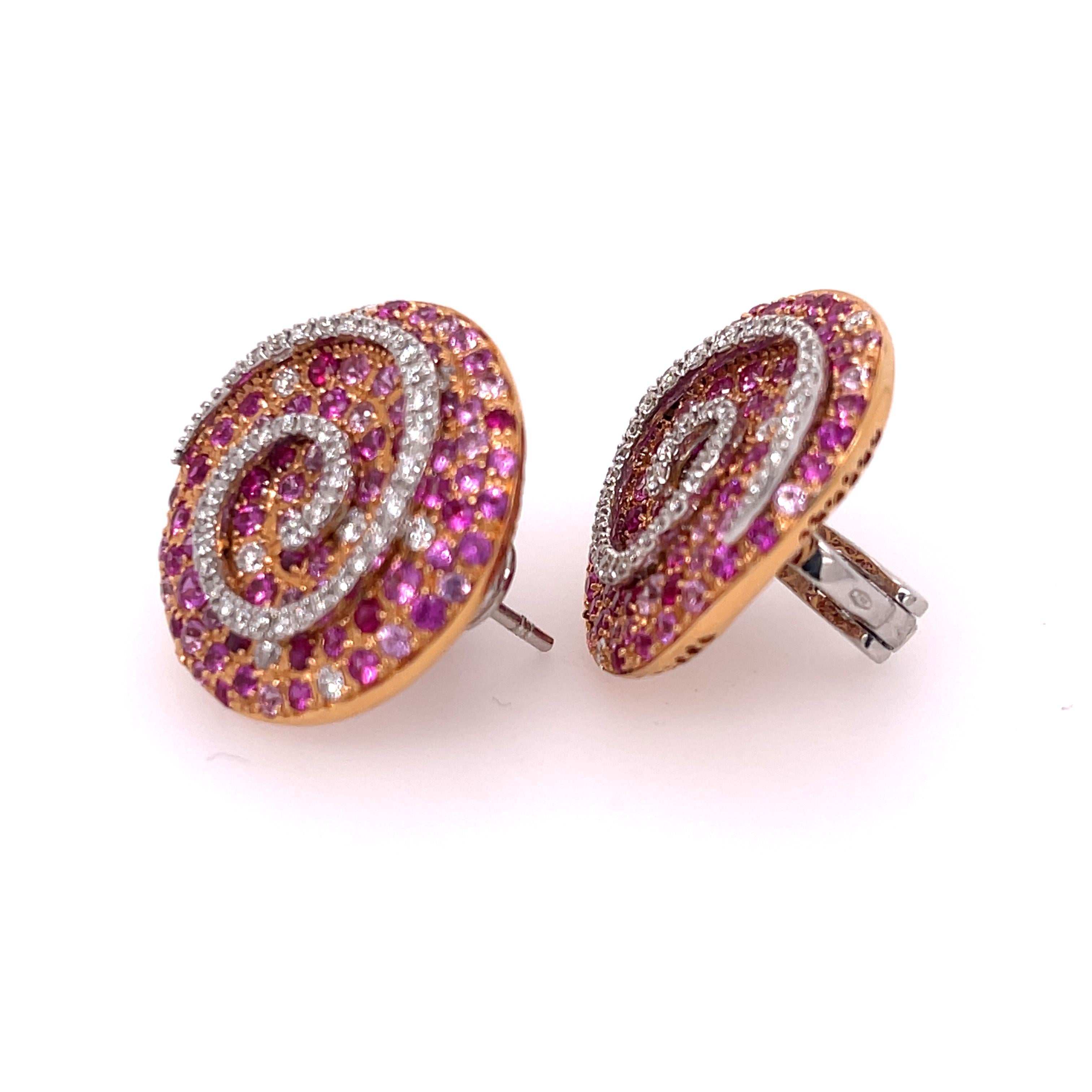 Ugo Cala ring with 3.79ctw of ruby and pink sapphires, 0.78ctw of diamonds, set in 18K rose and white gold. These captivating earrings each feature a disk of pave set rubies and pink sapphires with a swirl of diamonds running through it. This