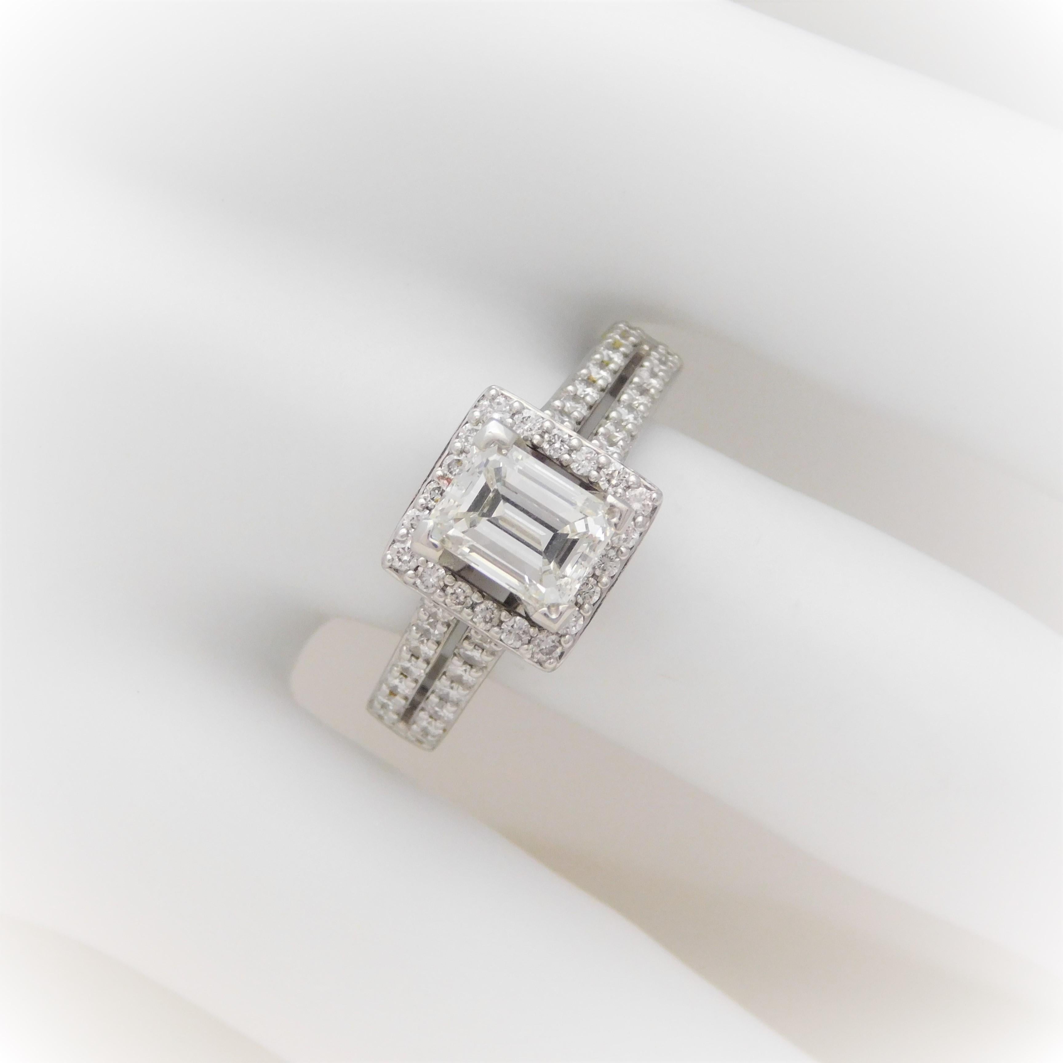 This stunning halo-style engagement ring has been crafted in solid 14k white gold.  It has been masterfully set, in a four-prong diamond halo setting, with a pristine 1.30ct emerald-cut natural diamond.  This high quality near colorless center