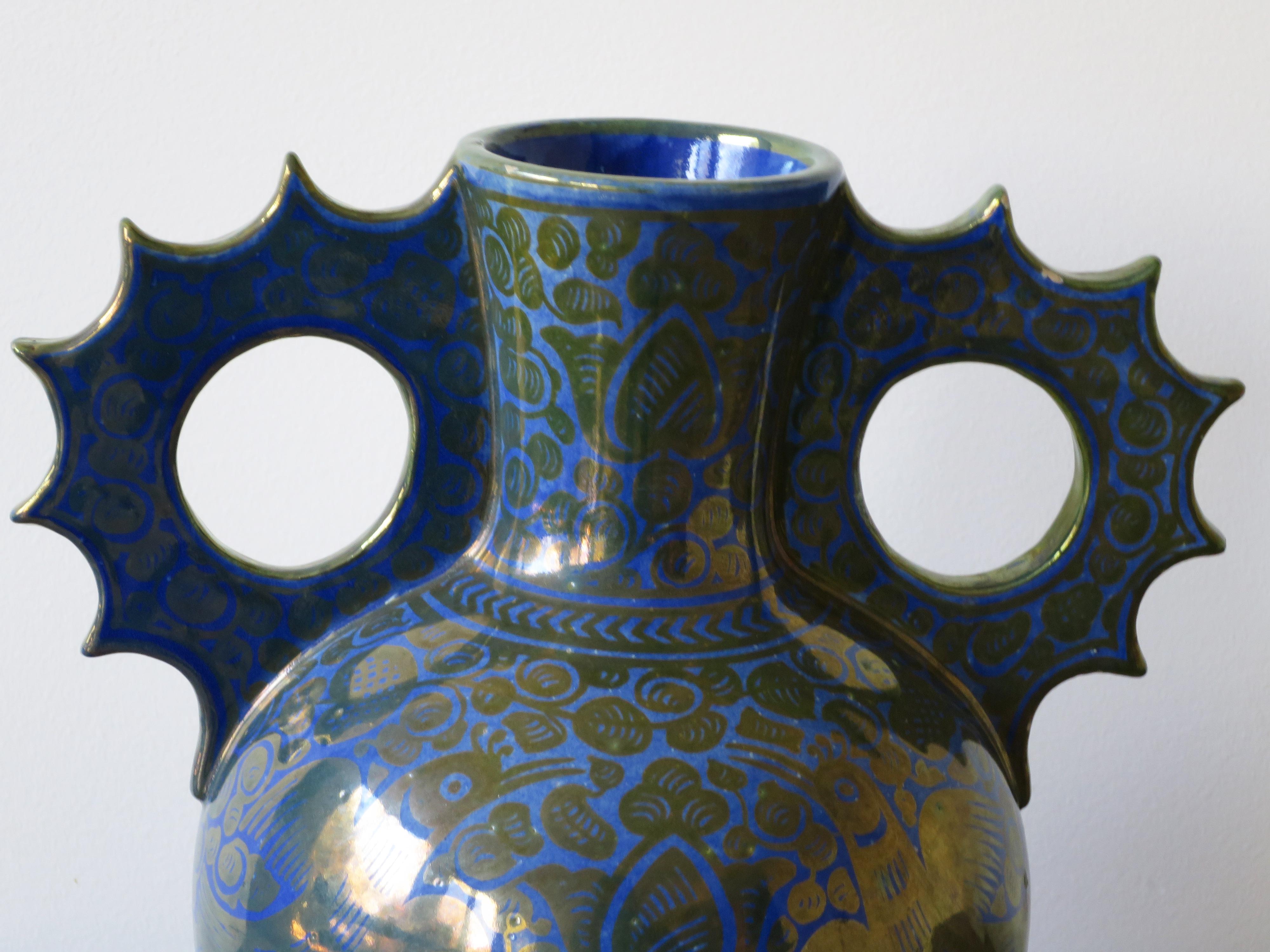 Signed with the mark of the rooster, the Cantagalli trademark, this vase has a silver mother of pearl glaze over blue ground. It is in the Hispano-Moresque style, with strikingly decorative handles in the Alhambra style. Cantagalli was friends with
