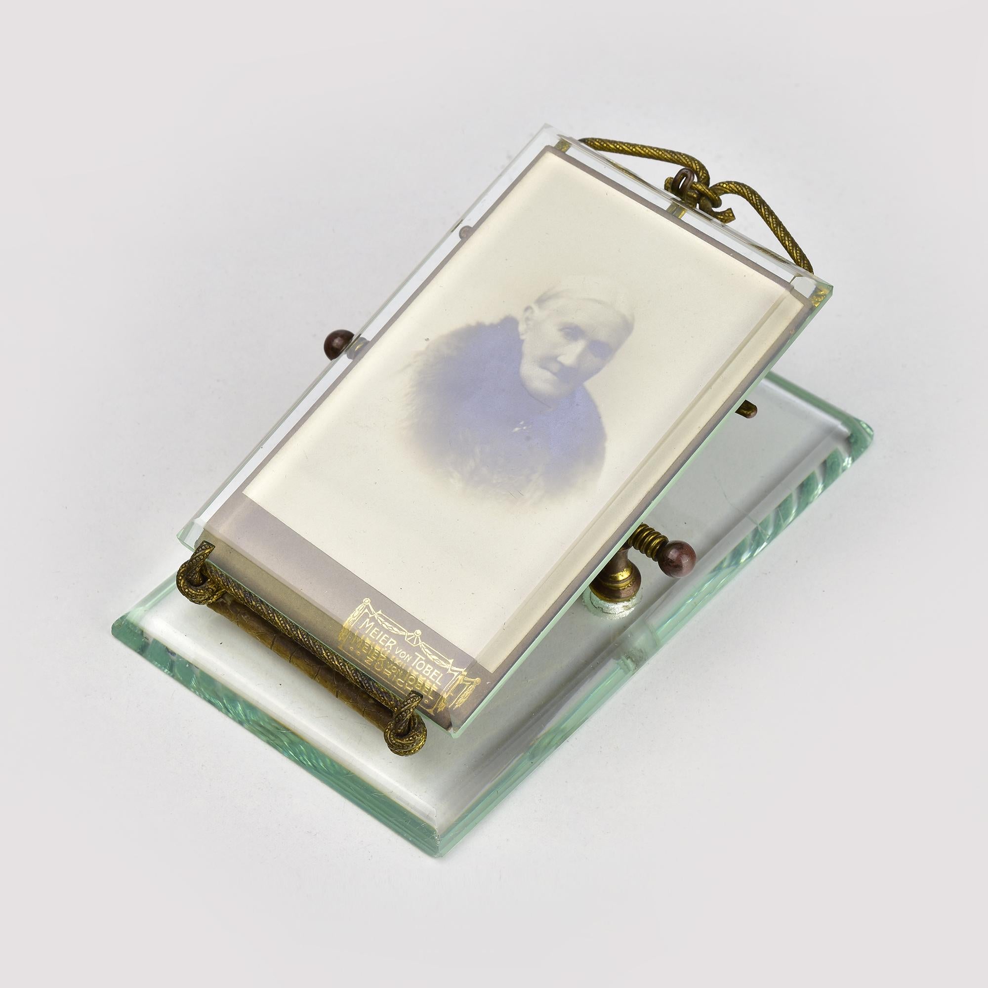 This ultra-rare picture frame clip, designed as a paperweight, dates back to around 1900. It features a beautifully crafted glass frame that can hold a photograph, with a distinct antique charm. 

The frame is elevated on a sturdy base made of