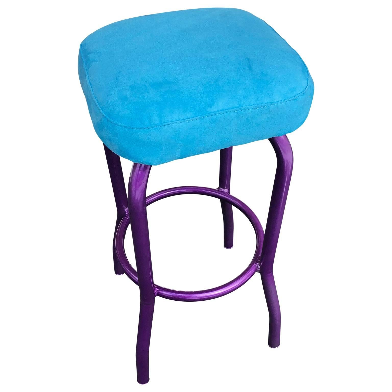 Bar stool powder coated ultra violet bar stool with newly upholstered blue faux suede seat.
Oh, this is fun and bold. The metal base has been powder coated in ultra violet and the seat is comfortable and bright in turquoise. As a single piece in a