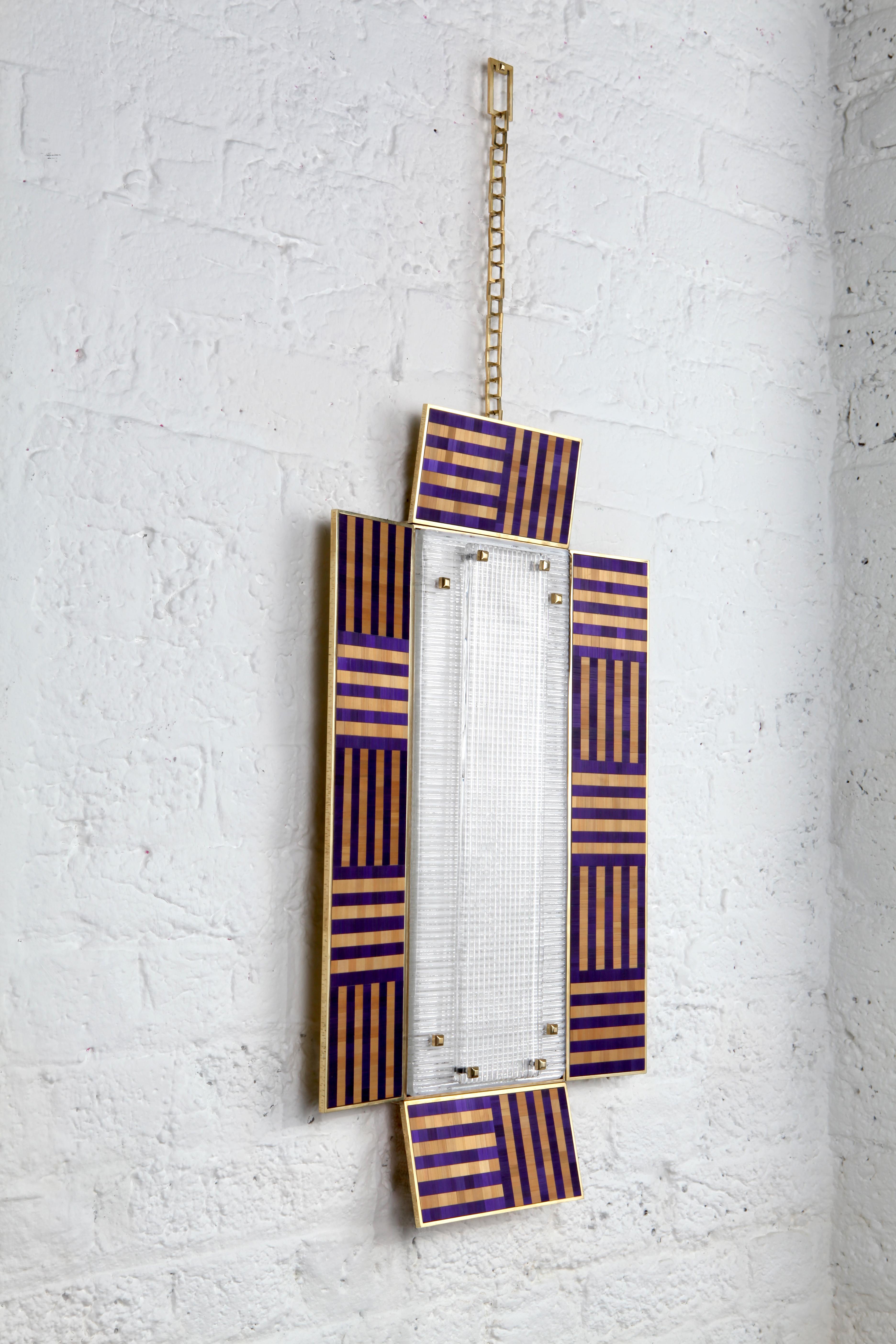 The ultra violet wall sconce is taken from Charles Burnand's Icon's collection. It features a panel of handcrafted Murano glass, set within a hammered brass frame. The surrounding panels are made using a straw marquetry finish in vibrant violet and