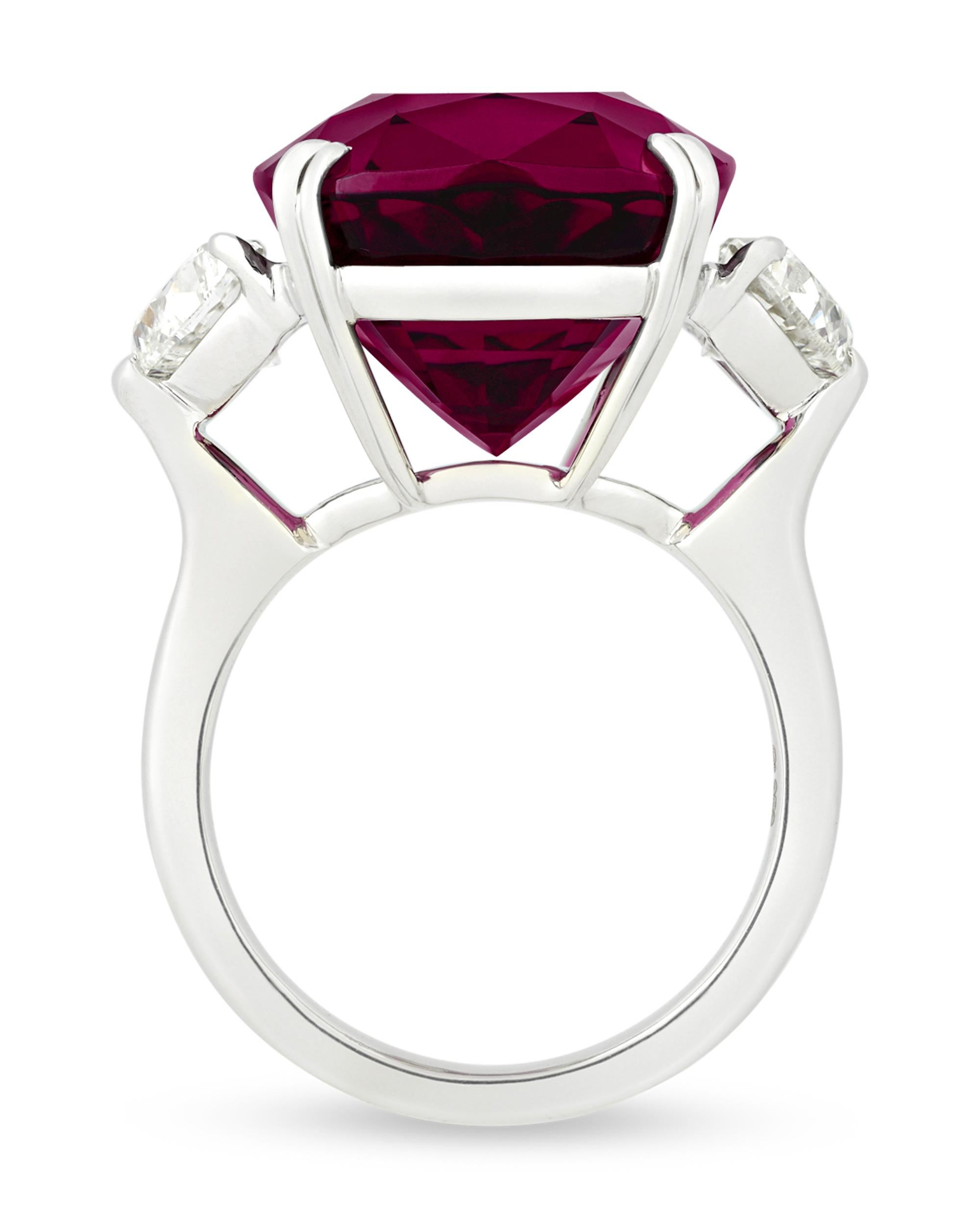 A smoldering Umbalite garnet centers this dramatic ring. Weighing an astounding 26.50 carats, the gemstone displays a radiant, deep raspberry hue that exudes a regal femininity. Classically set in platinum, the stone is complemented by two