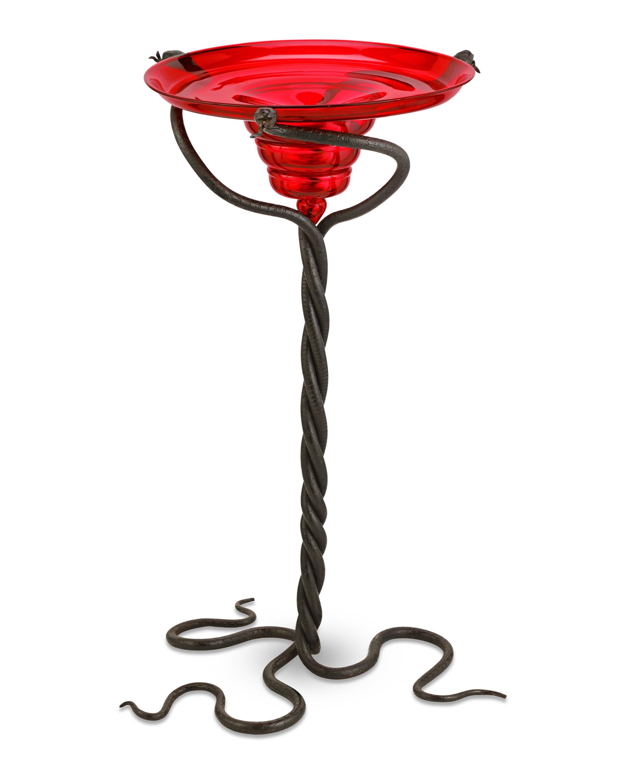 This bold and unique serpentiform pedestal table is the work of renowned Italian artisan Umberto Bellotto. The creative design twists three slithering snake-shaped wrought-iron rods together to form a supportive base for an eye-catching red Venetian
