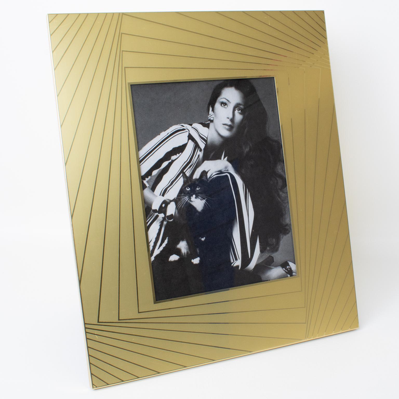 El diseñador italiano Umberto Mascagni, de Bolonia, diseñó este fascinante marco de fotos en la década de 1970. La pieza es de aluminio dorado con un diseño brillante y esmerilado y rayos de sol. La parte trasera y el caballete son una patente