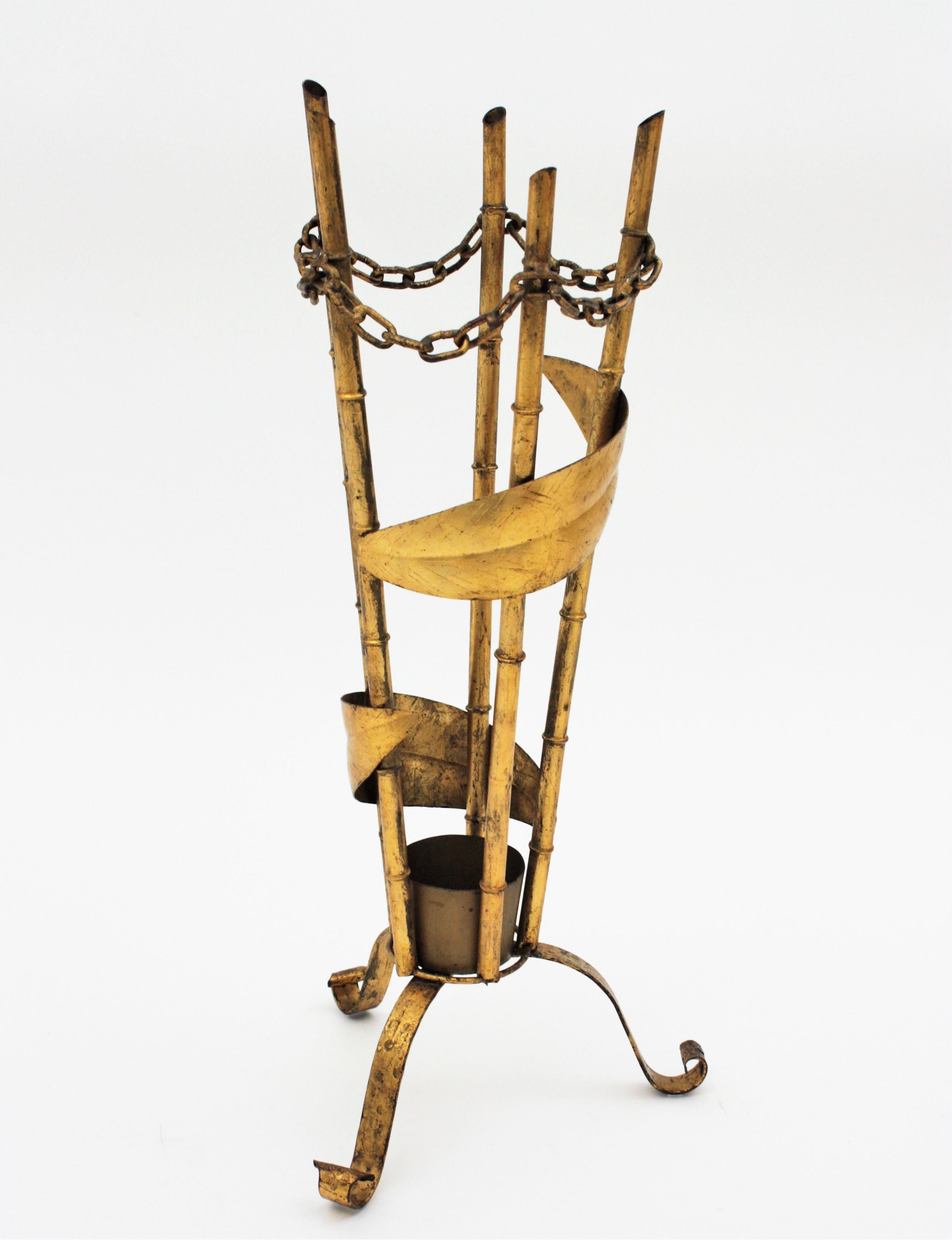 Nice gilt wrought iron faux bamboo umbrella stand with chain link accents. Spain, 1940s-1950s.
This hand forged umbrella stand features a tripod base holding a faux bamboo iron sctructure ornamented with chain-link and leaf accents. It has a