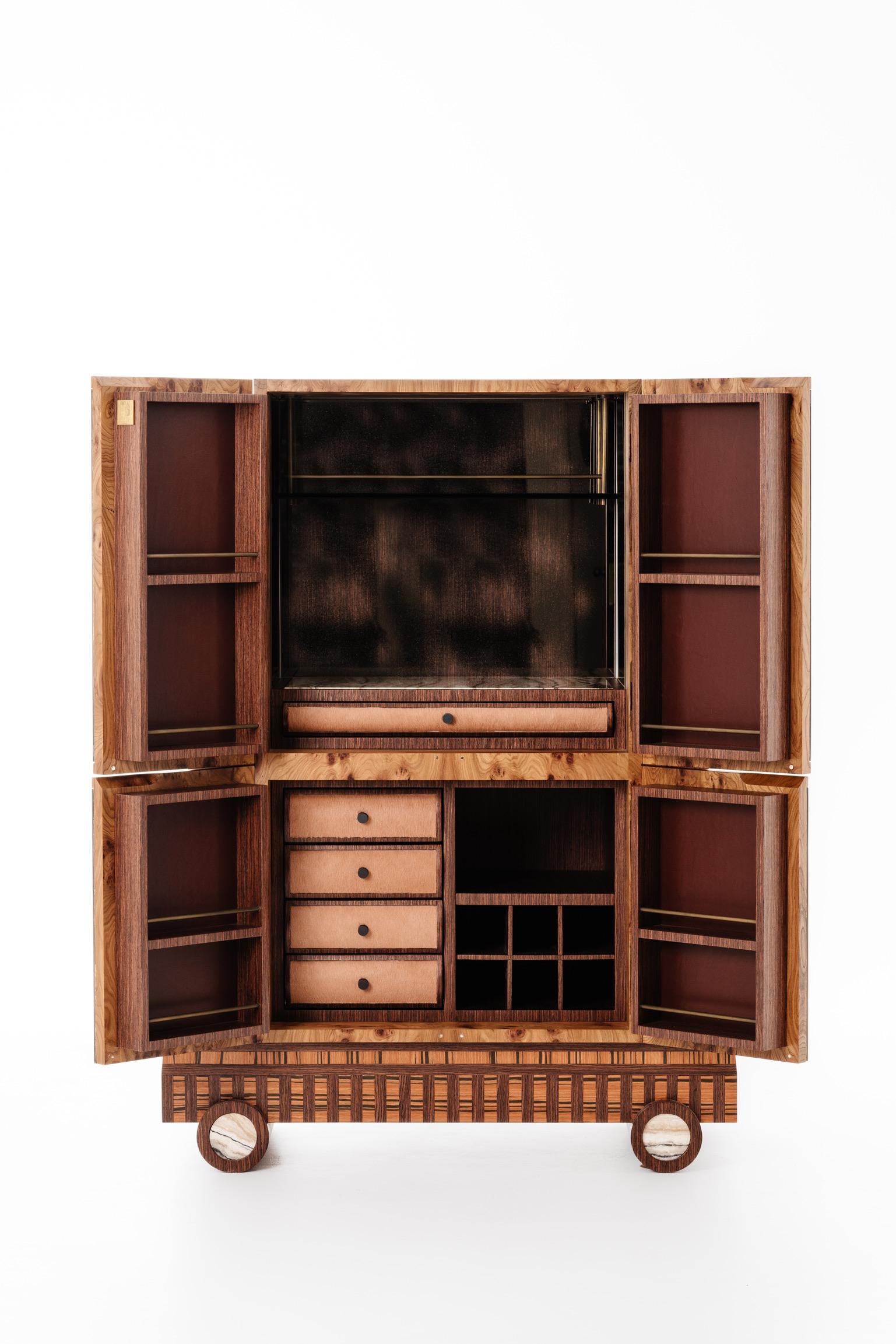 The graphic layering of exotic burled and cathedral grained woods create the elevated “locker” bar cabinet. Interiors are adorned in woods, hand-woven leather, a touch of onyx and the most exquisite eglomise mirror cladding the interiors walls.