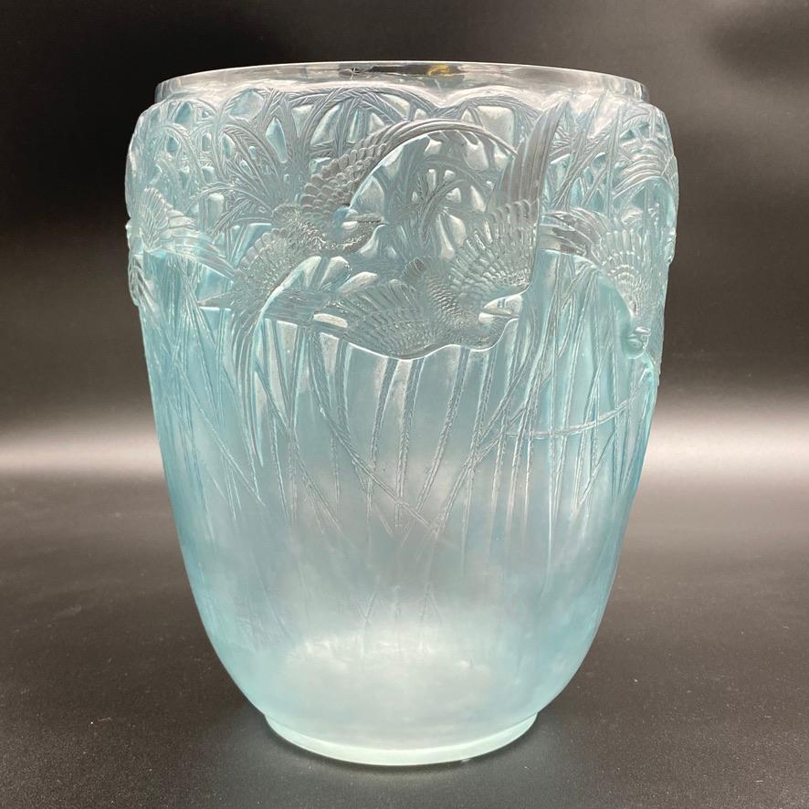 A large glass vase Aigrettes by R.lalique in white glass with a blue patina.

This design is probably one of the bests of Lalique and famous for its representation of flying birds on their roots back ground around the vase's body.

The vase is