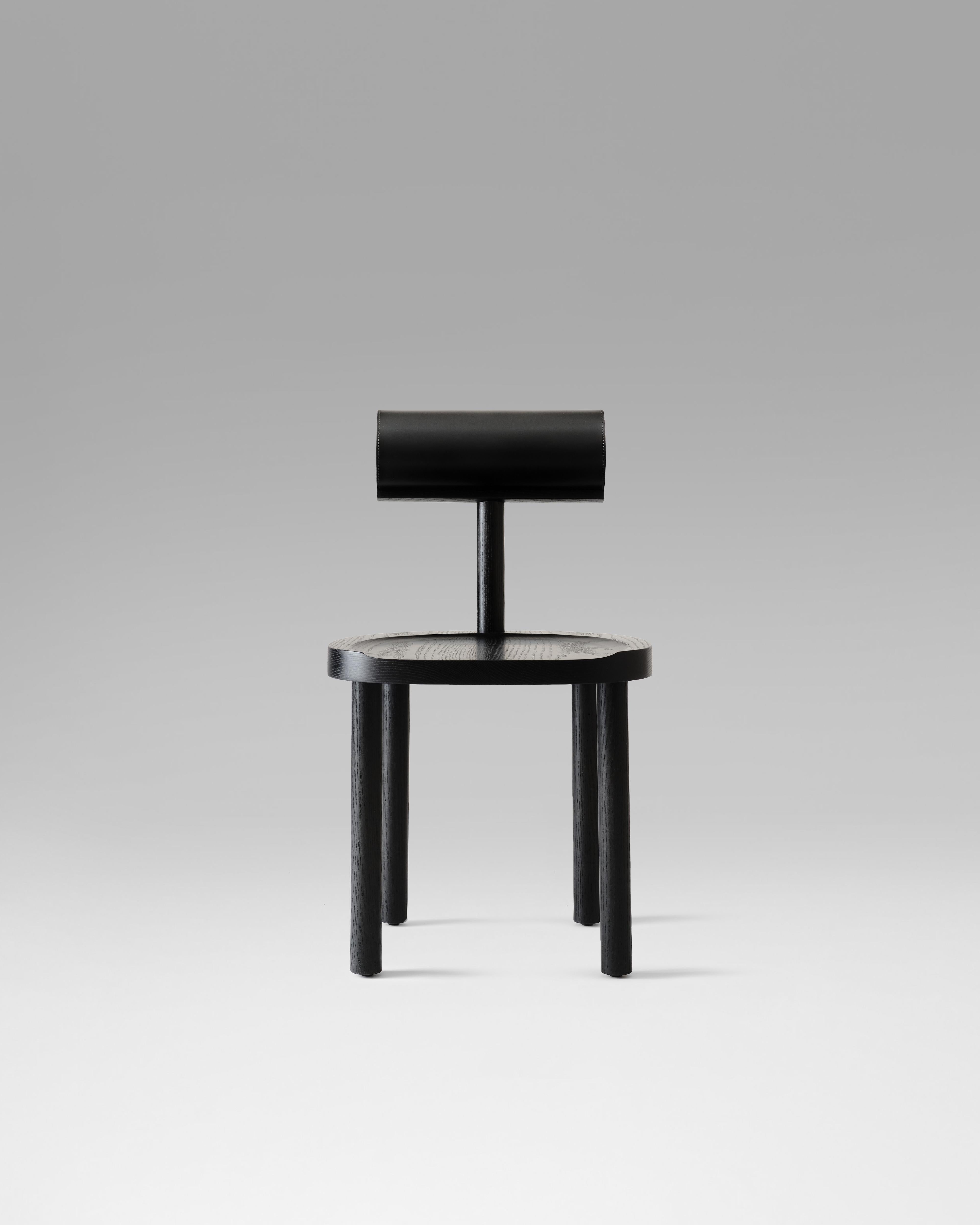 The UNA chair combines a curved wooden seat and legs with a leather-upholstered cylindrical back, creating a balance between comfort and simple geometry. Its design highlights the natural beauty of the wood grain and emphasizes the craftsmanship of