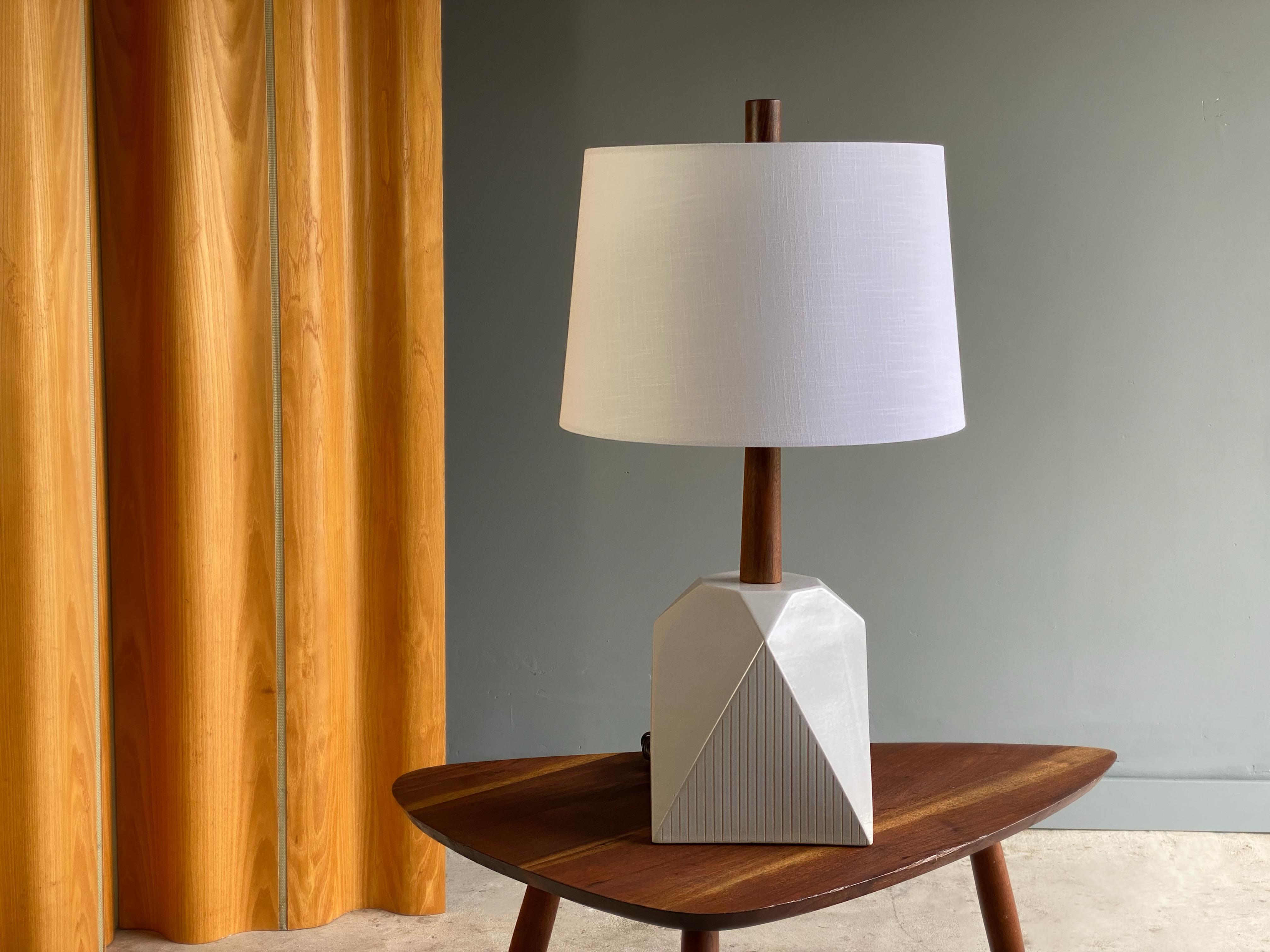 Uncommon geometric ceramic table lamp by talented Gordon and Jane Martz for Marshall studios. This example features incised vertical detailing on a lovely white glaze body with walnut neck and finial. Unique form that changes its appearance when