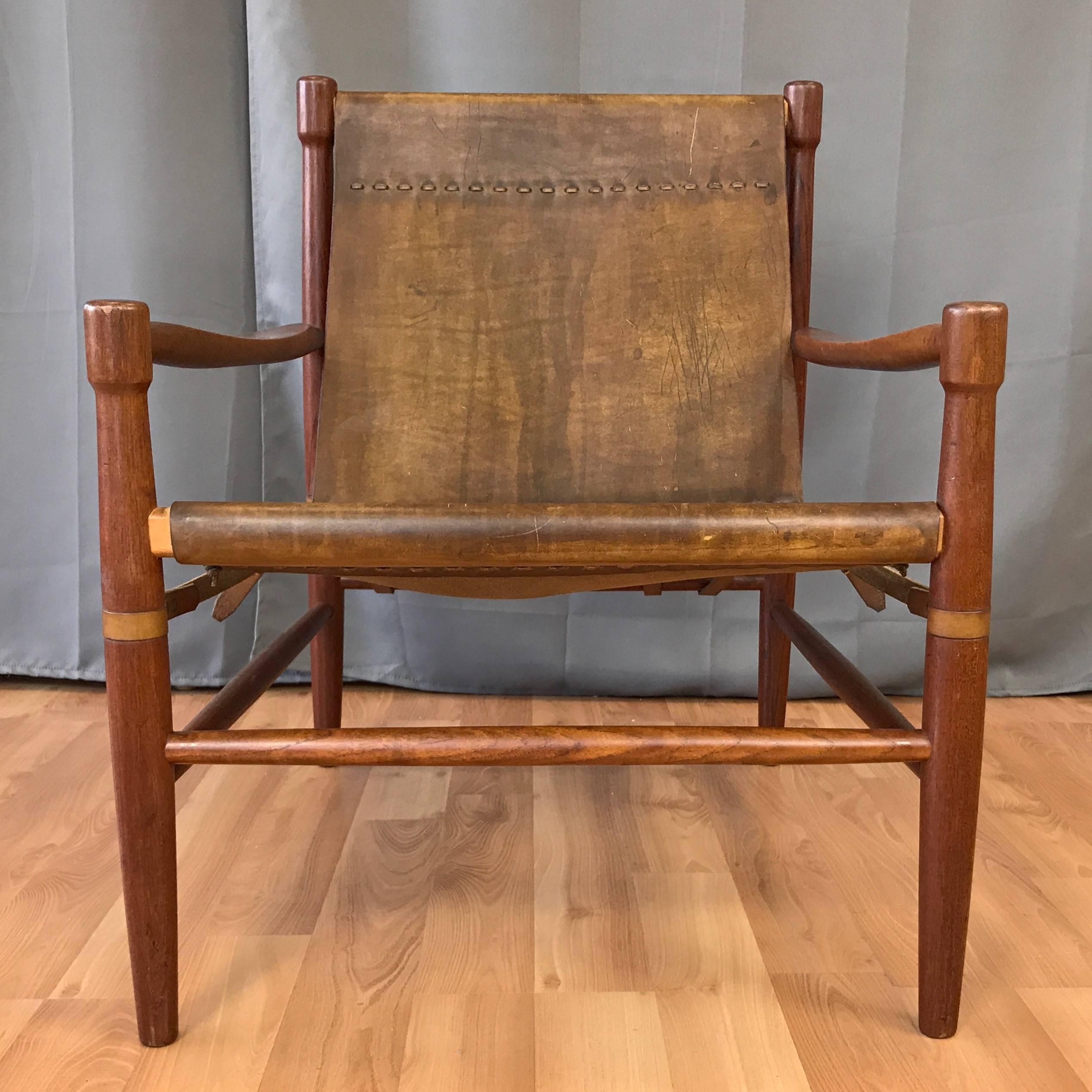 An uncommon Danish teak and leather safari chair in the manner of Kaare Klint, Erik Worts, or Arne Norell.

Solid teak frame with sculpted arms and distinctive drumstick legs. Original dark tan sling seat is a single piece of thick, weathered