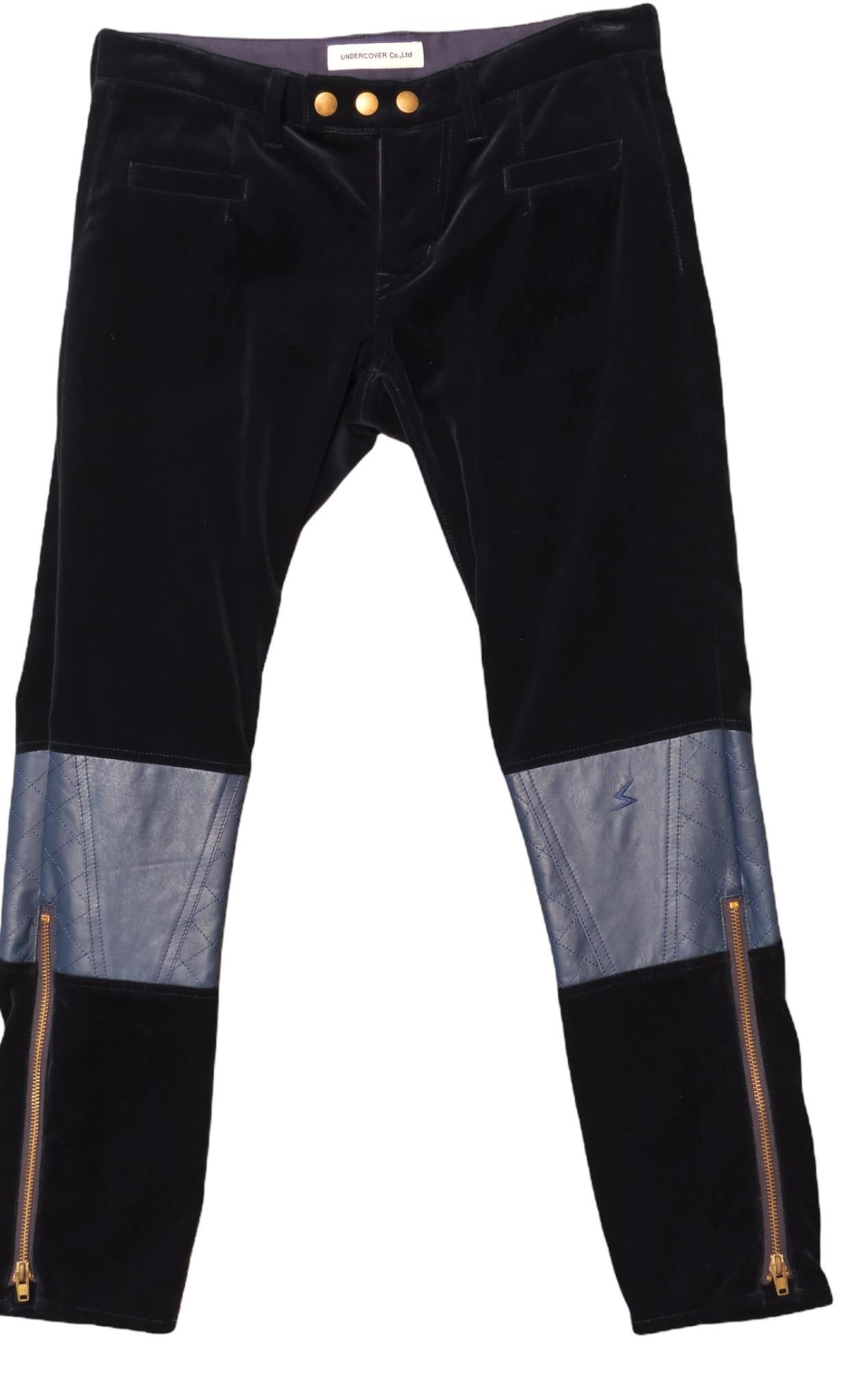 Pantalon droit vintage Undercover de couleur marine, velouté et doux, avec empiècements en cuir aux genoux et jambes zippées. Fermeture à glissière et boutons-pression sur le devant, avec poches avant et arrière.